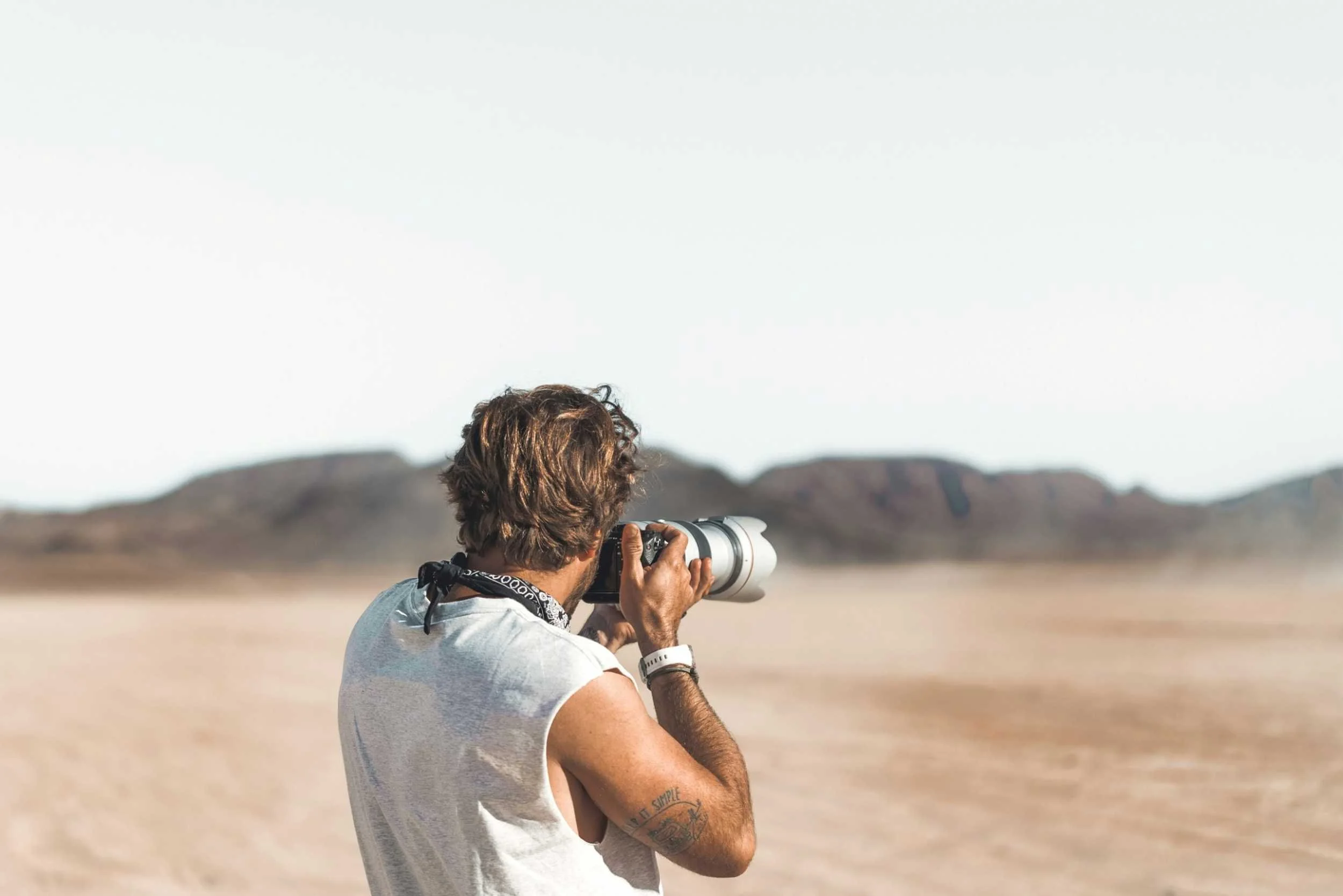 Man with tattoo holds camera in desert
