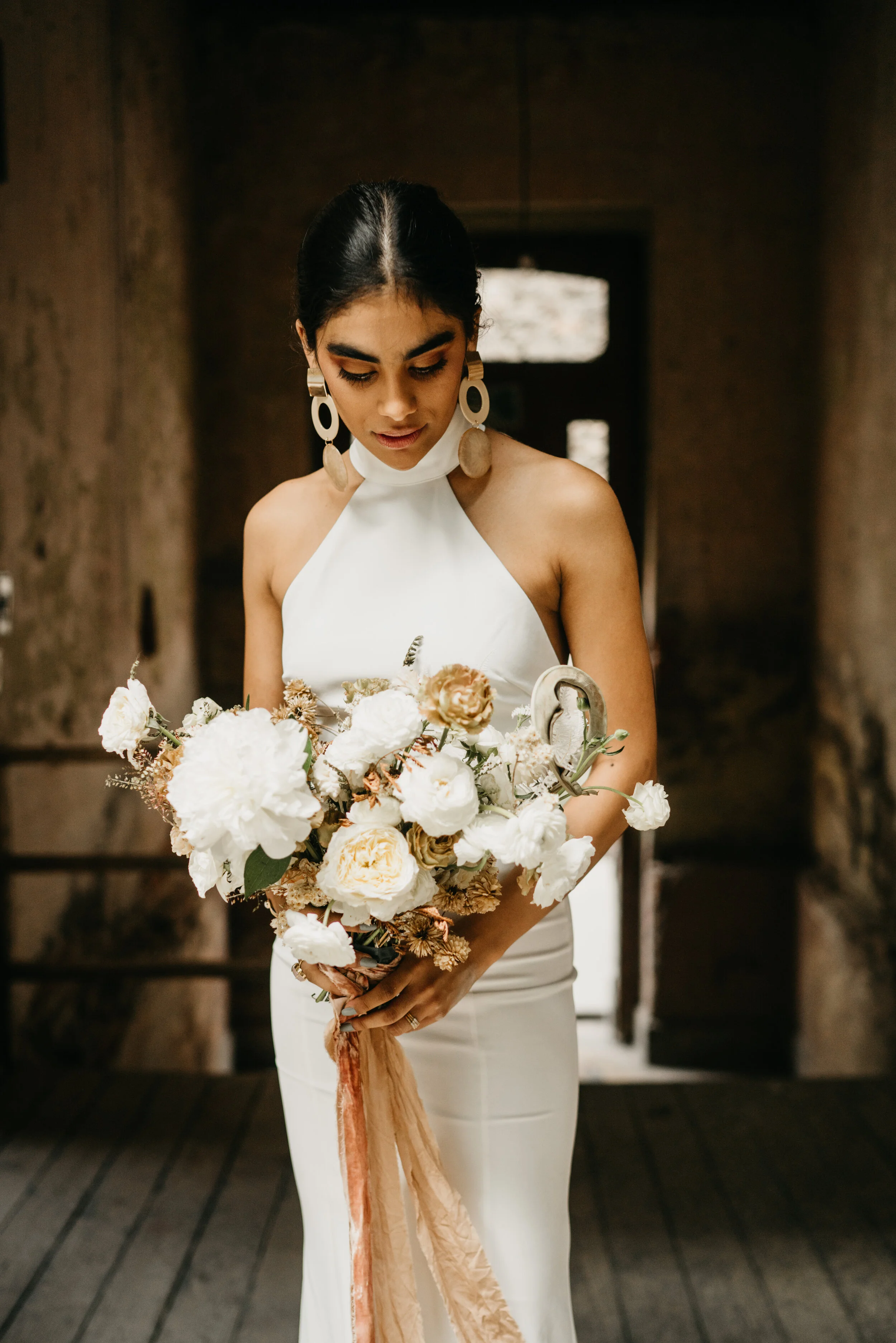 A woman in a white dress holding a bouquet of white and beige flowers indoors.