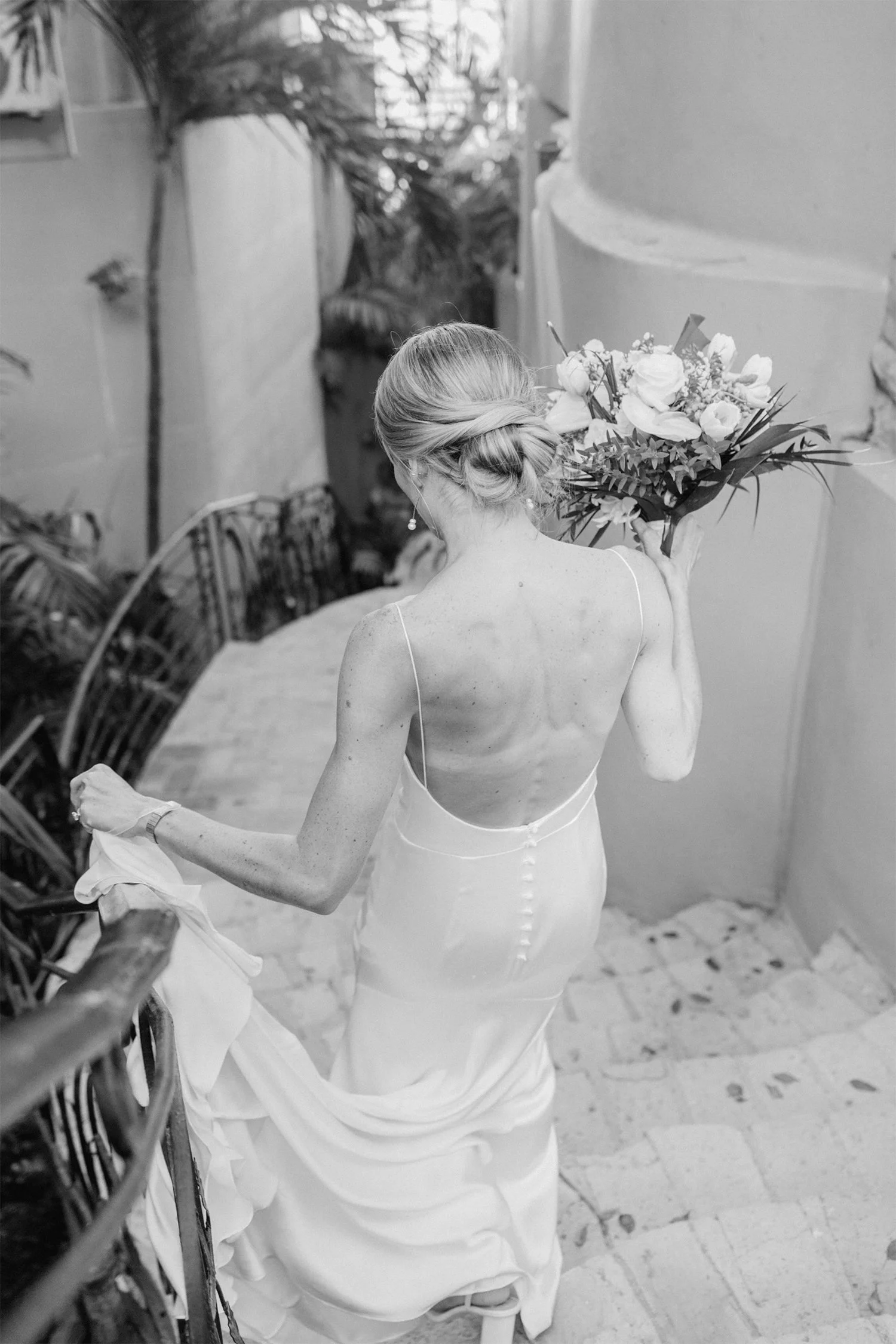 A woman in a wedding dress carrying a bouquet of flowers walking down stairs.