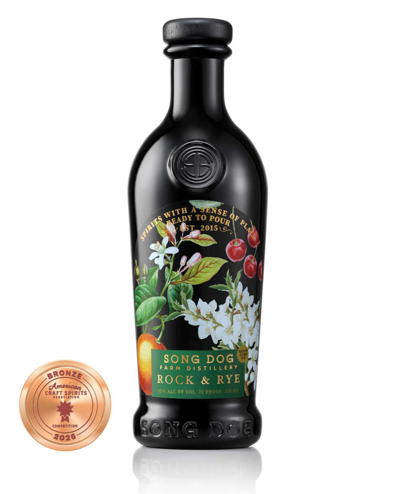 A black bottle of Song Dog Rock & Rye with a label featuring cherries, white flowers, and green leaves, along with an award medal from the American Craft Spirits Association.