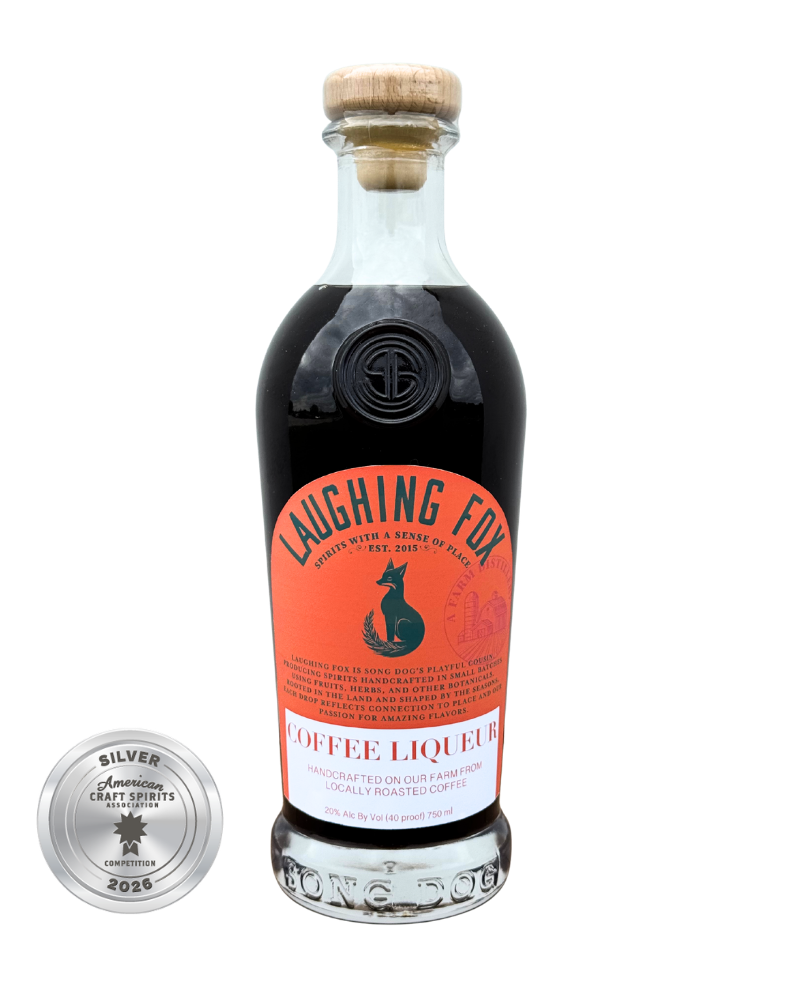 A bottle of Laughing Fox Coffee Liqueur with a wooden cork and a black and orange label featuring a fox silhouette. A silver medal from the American Craft Spirits Association competition in 2026 is shown next to the bottle.