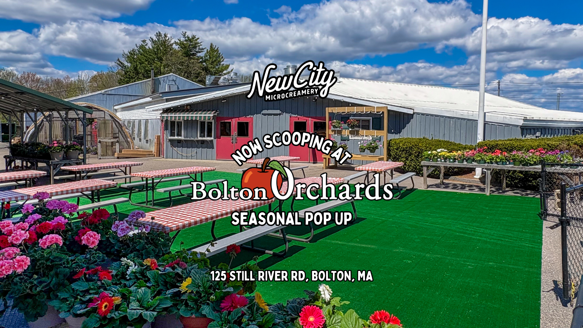 Outdoor seating area with pink and white checkered tablecloths, benches, and potted flowers in front of a blue building with a sign for New City Microcreamery, Bolton Orchards seasonal pop-up, located at 125 Still River Rd, Bolton, MA.