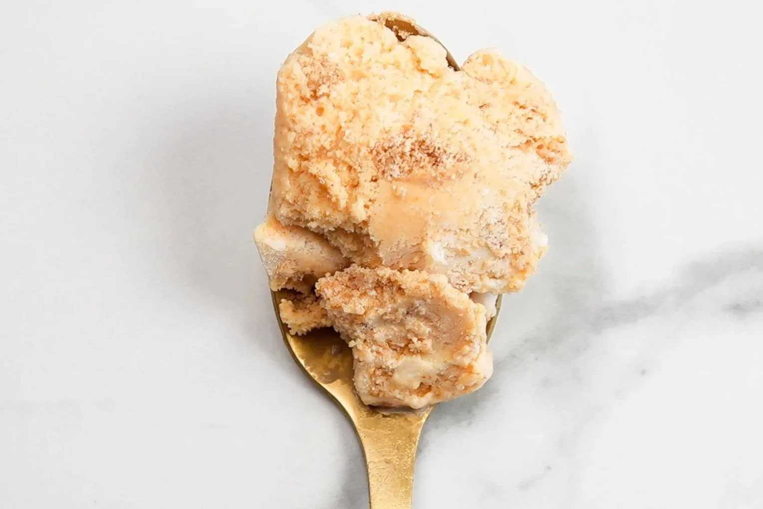 Slices of peach cobbler topping on a gold spoon, on a white marble surface.