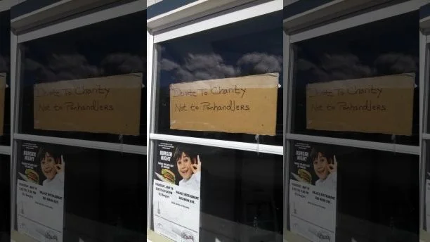 A cardboard sign urging people not to give to panhandlers directly.