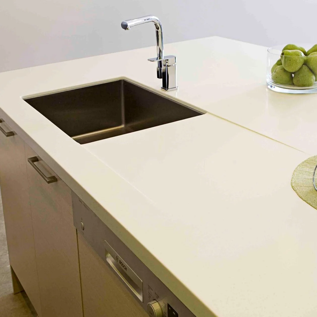 Kitchen countertop with stainless steel sink, chrome faucet, a bowl of green pears, and a dishwasher beneath.