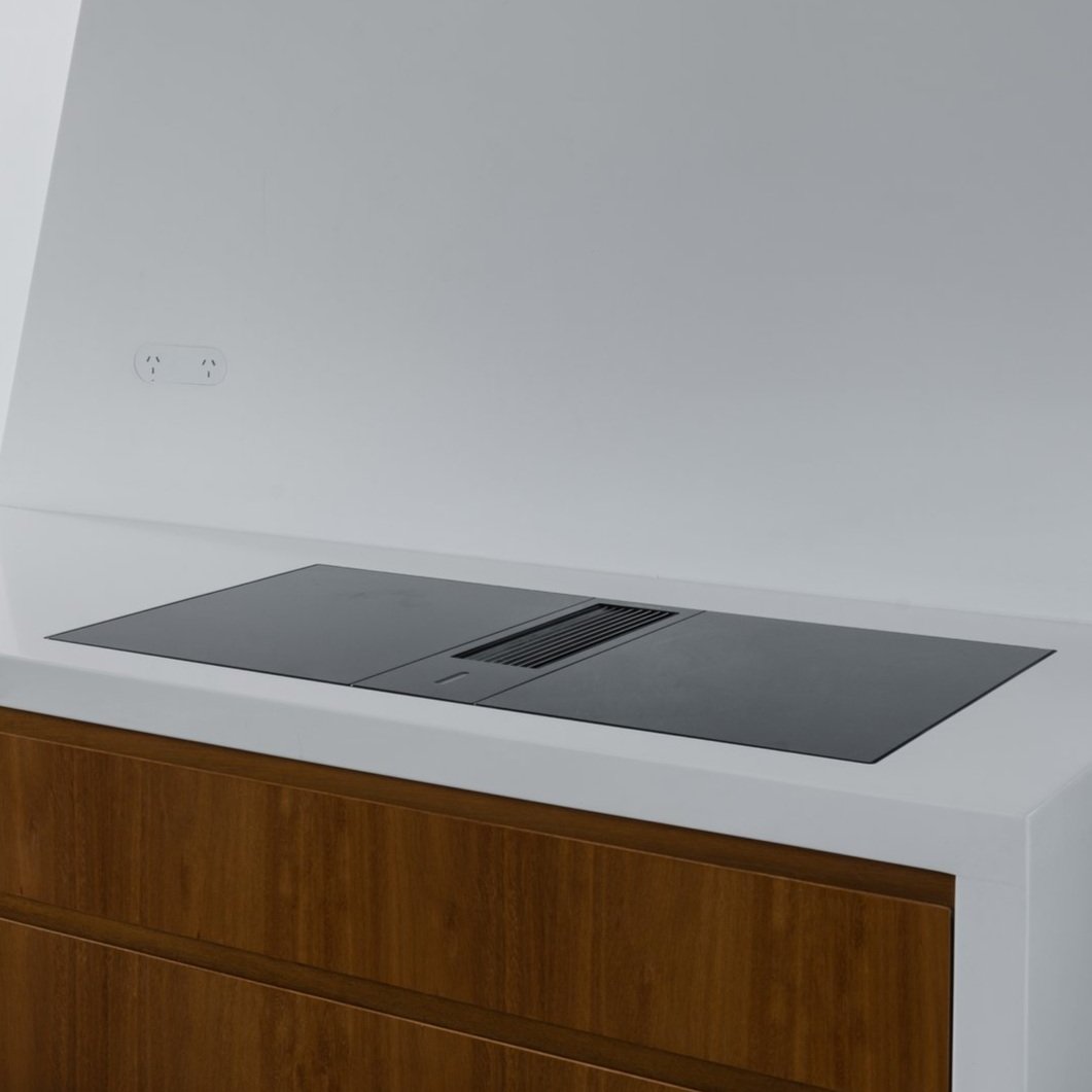 Close-up of a white surface with an electrical outlet, sitting above a wooden cabinet, with a black built-in speaker or sound system installed on the surface.