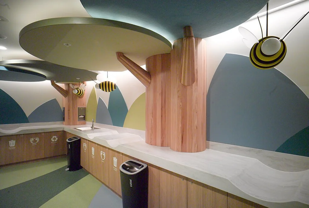 Children's play area or themed room with a large tree sculpture, decorated with bee and insect-shaped hanging decorations, and a colorful, abstract wall design.