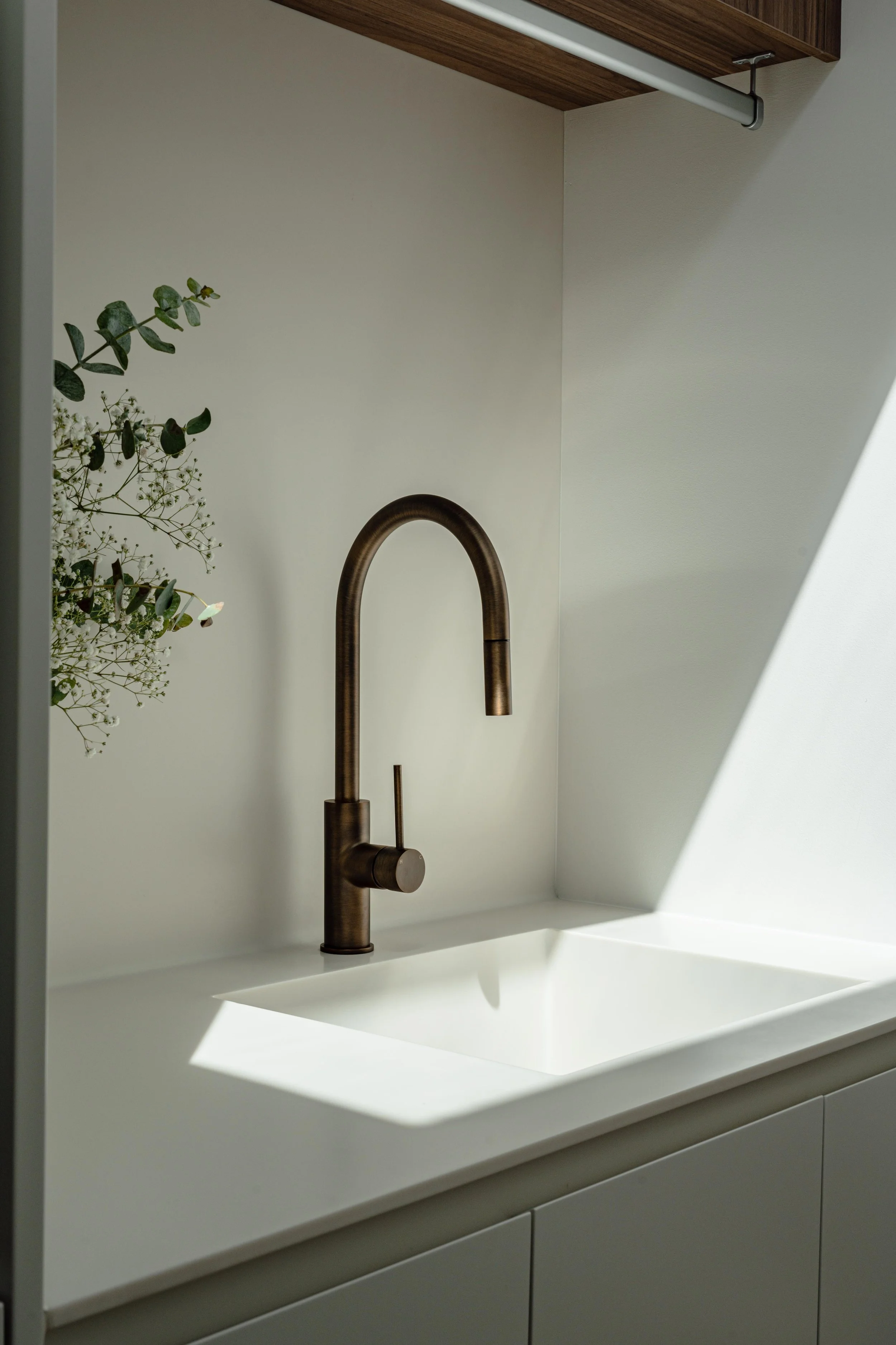 Kitchen sink with bronze faucet, white countertop, and a small plant on the left side.