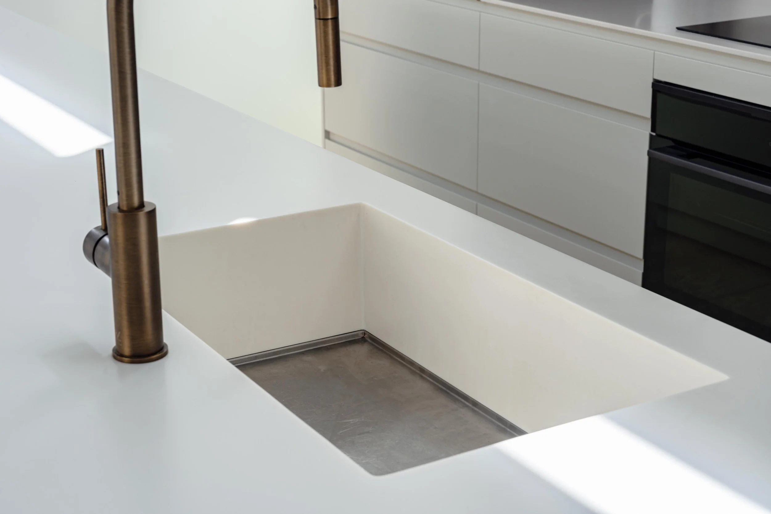 Modern kitchen sink with a white countertop and a brass faucet.