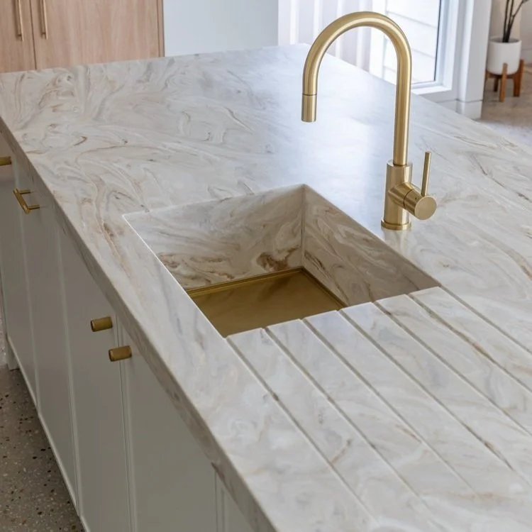 A kitchen sink with a marble countertop and a gold faucet.