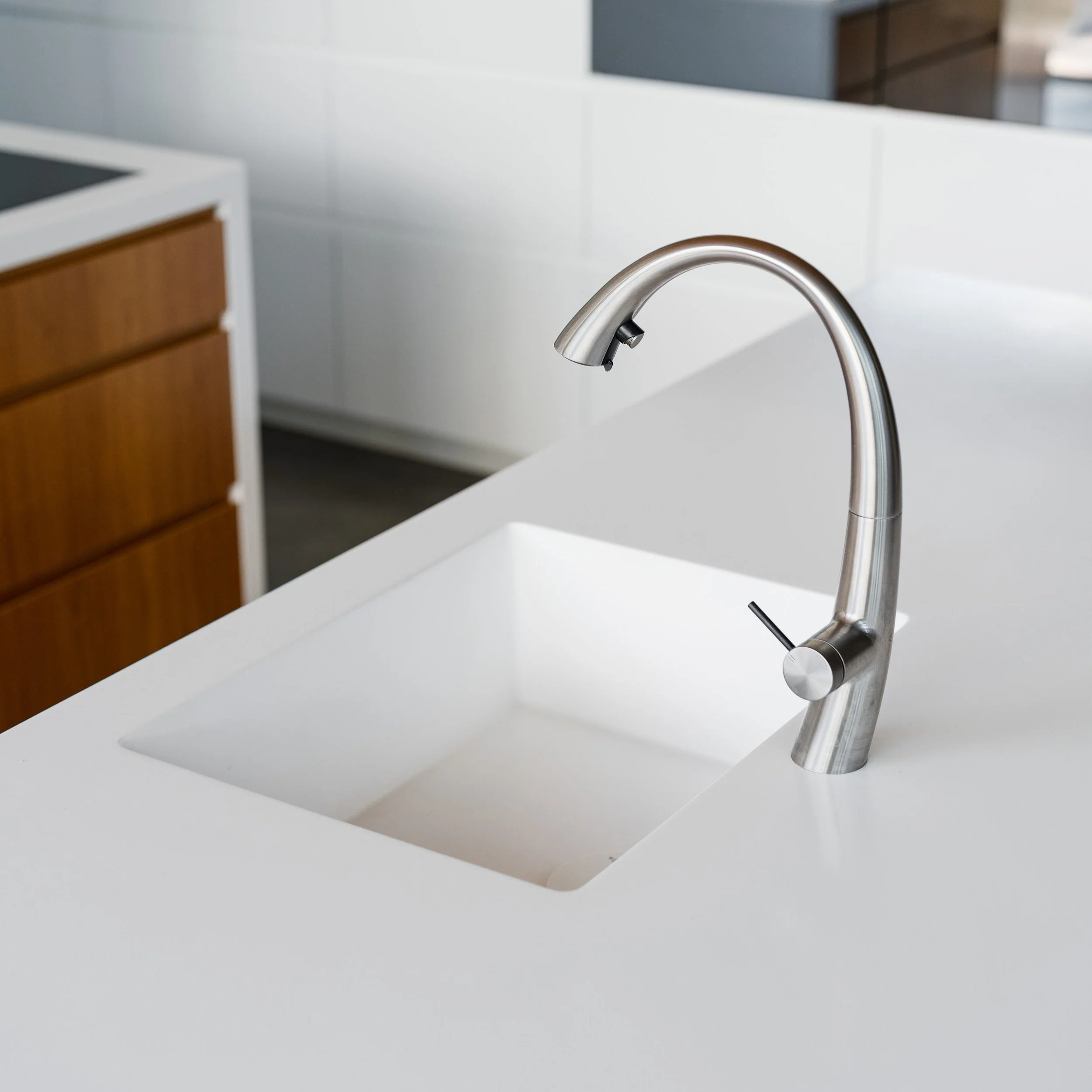 A modern kitchen sink with a curved stainless steel faucet installed on a white countertop.