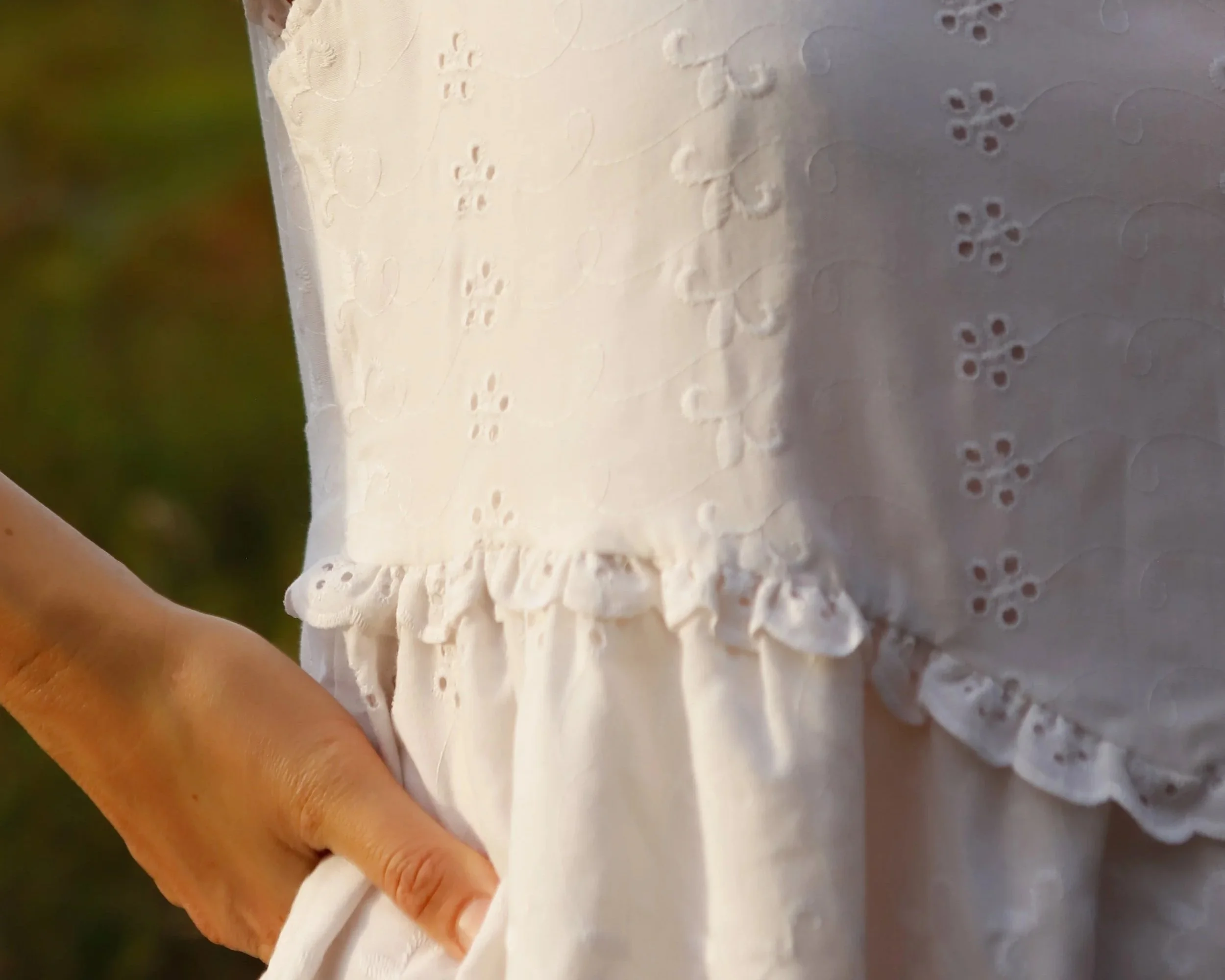 Close-up of a person's hand holding a white fabric with embroidered floral patterns.