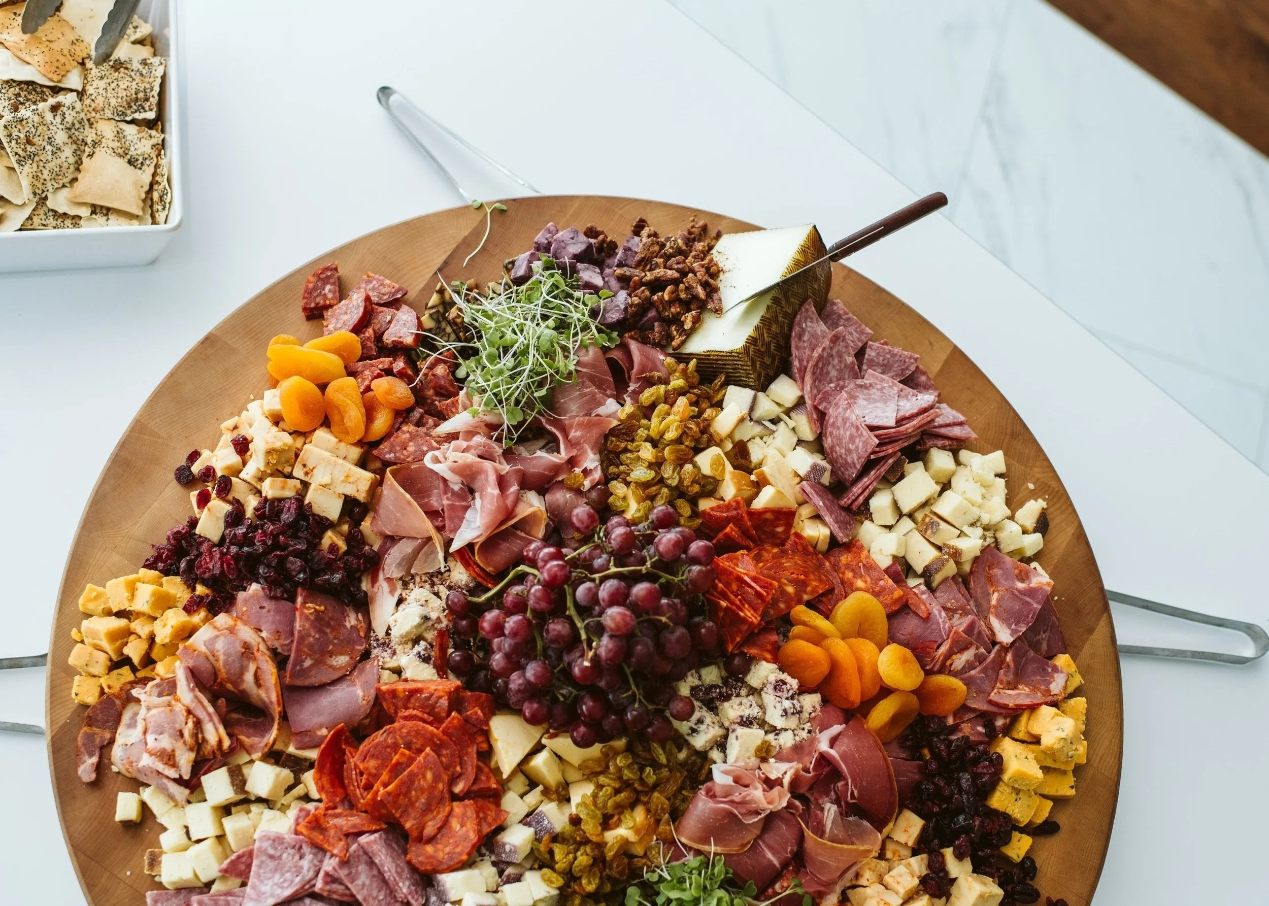 Assorted artisan cheeses, cured meats, grapes, dried apricots, and microgreens on a wooden charcuterie board - Chef Kansas City Catering