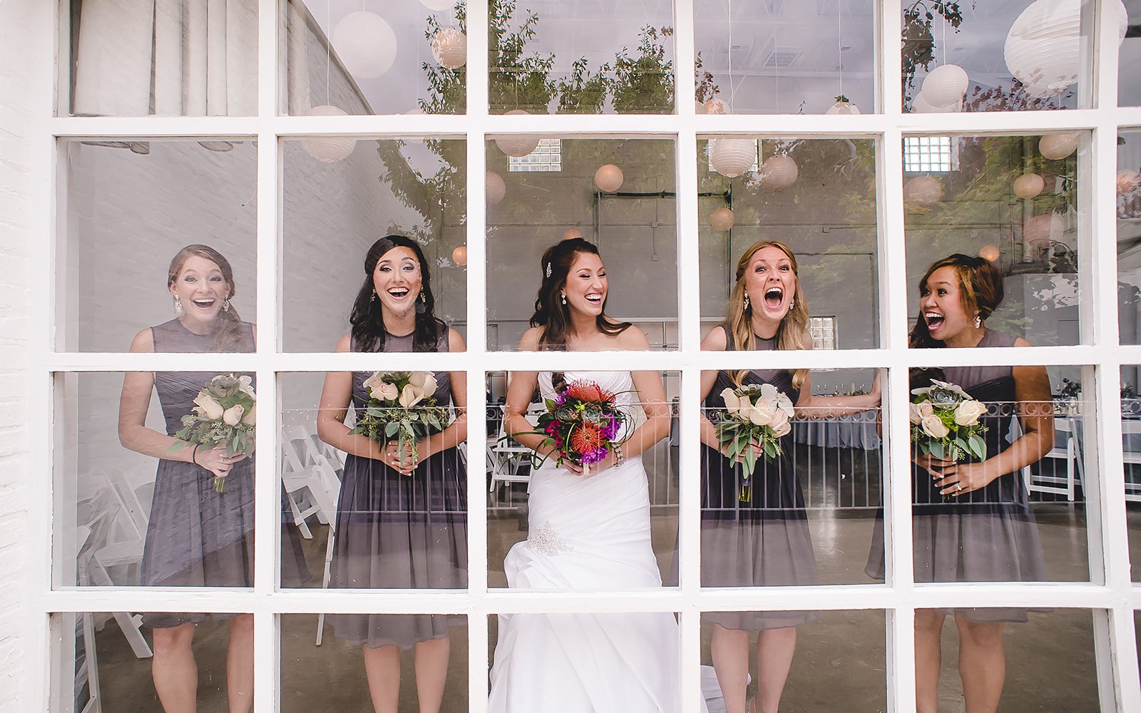  bride and her bridesmaids laughing by a window 