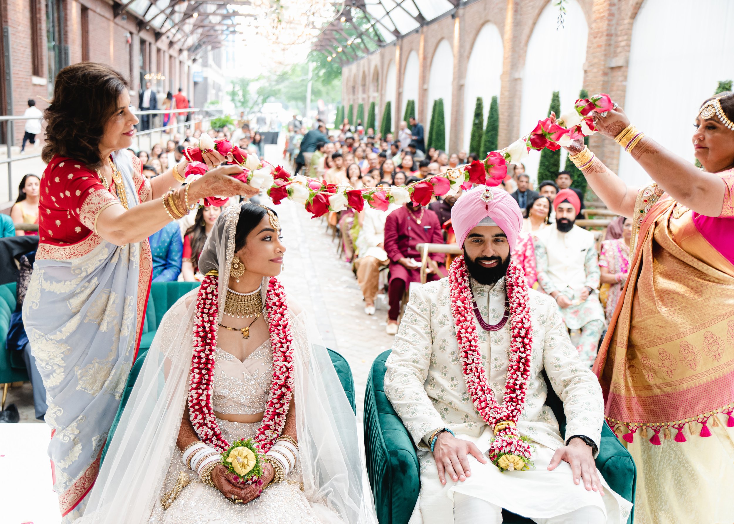  An Hindu Sikh fusion wedding ceremony: The couple shares an amused glance as their mothers lay flowers on them 