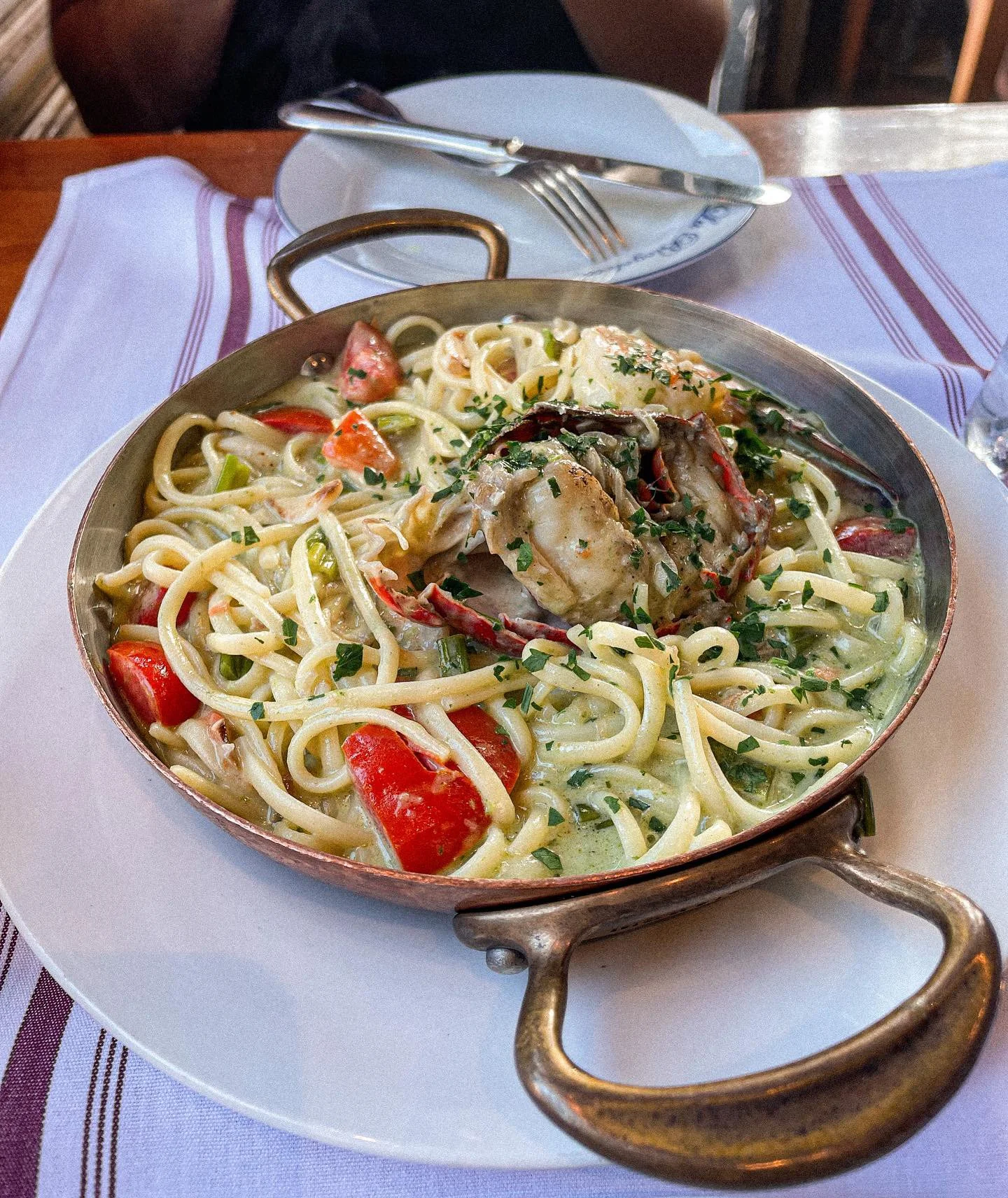 Seafood pasta with cherry tomatoes, herbs, and creamy sauce in a copper pan on a white plate