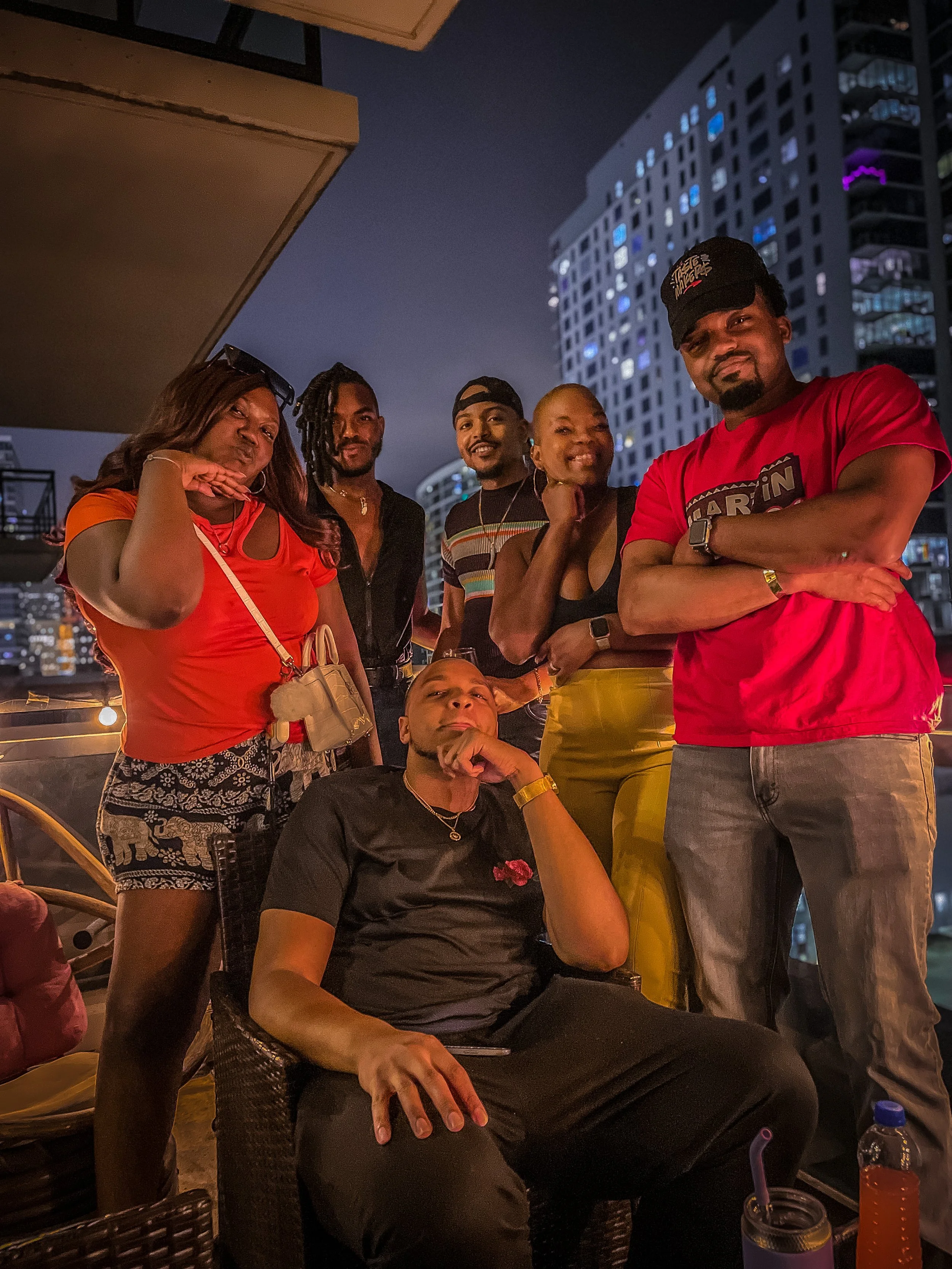 Group of six friends enjoying a night out on a rooftop terrace at night, with tall buildings illuminated in the background.