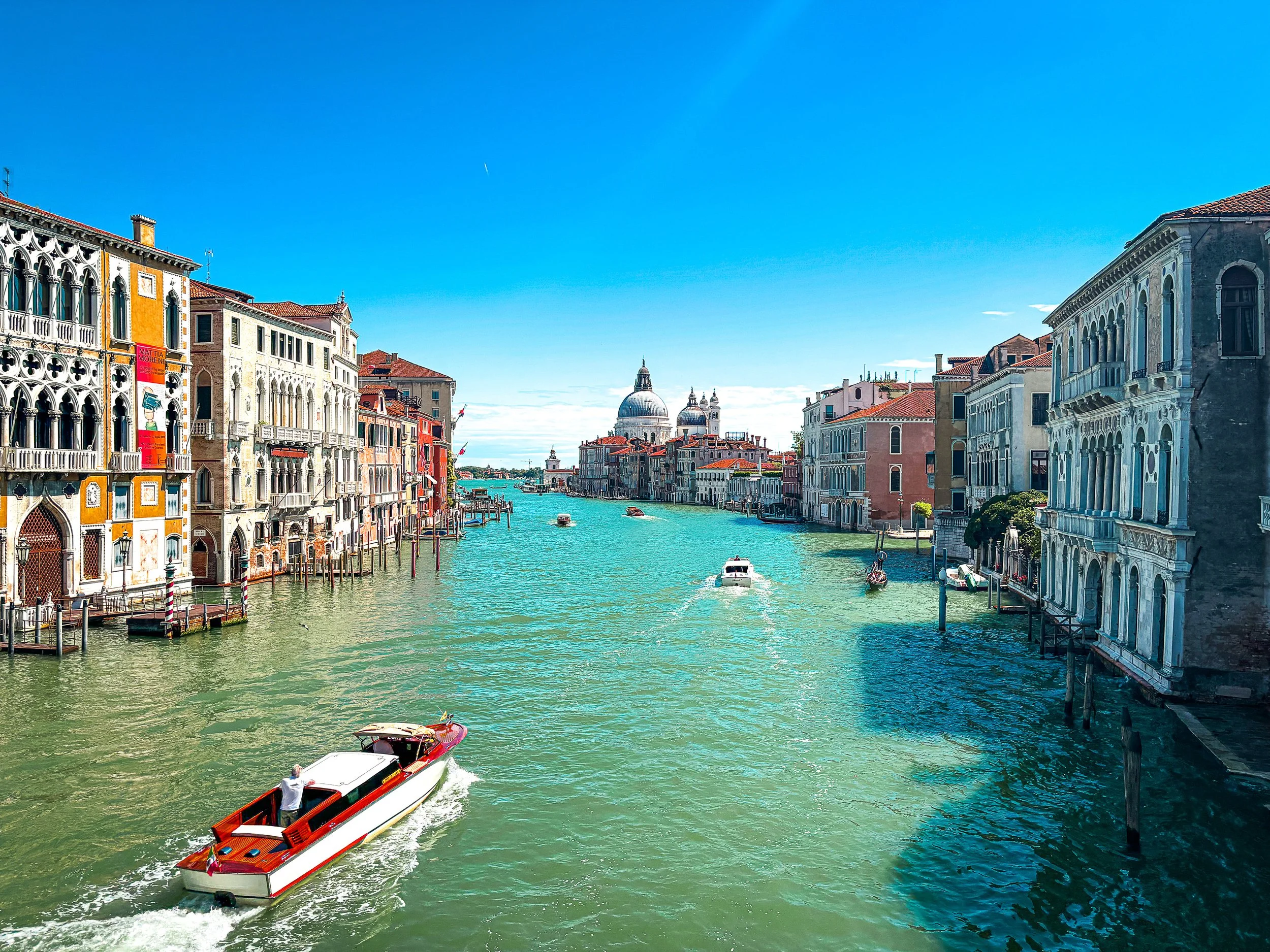 Venetian canal with colorful historic buildings on both sides, a boat in the water, and a clear blue sky.
