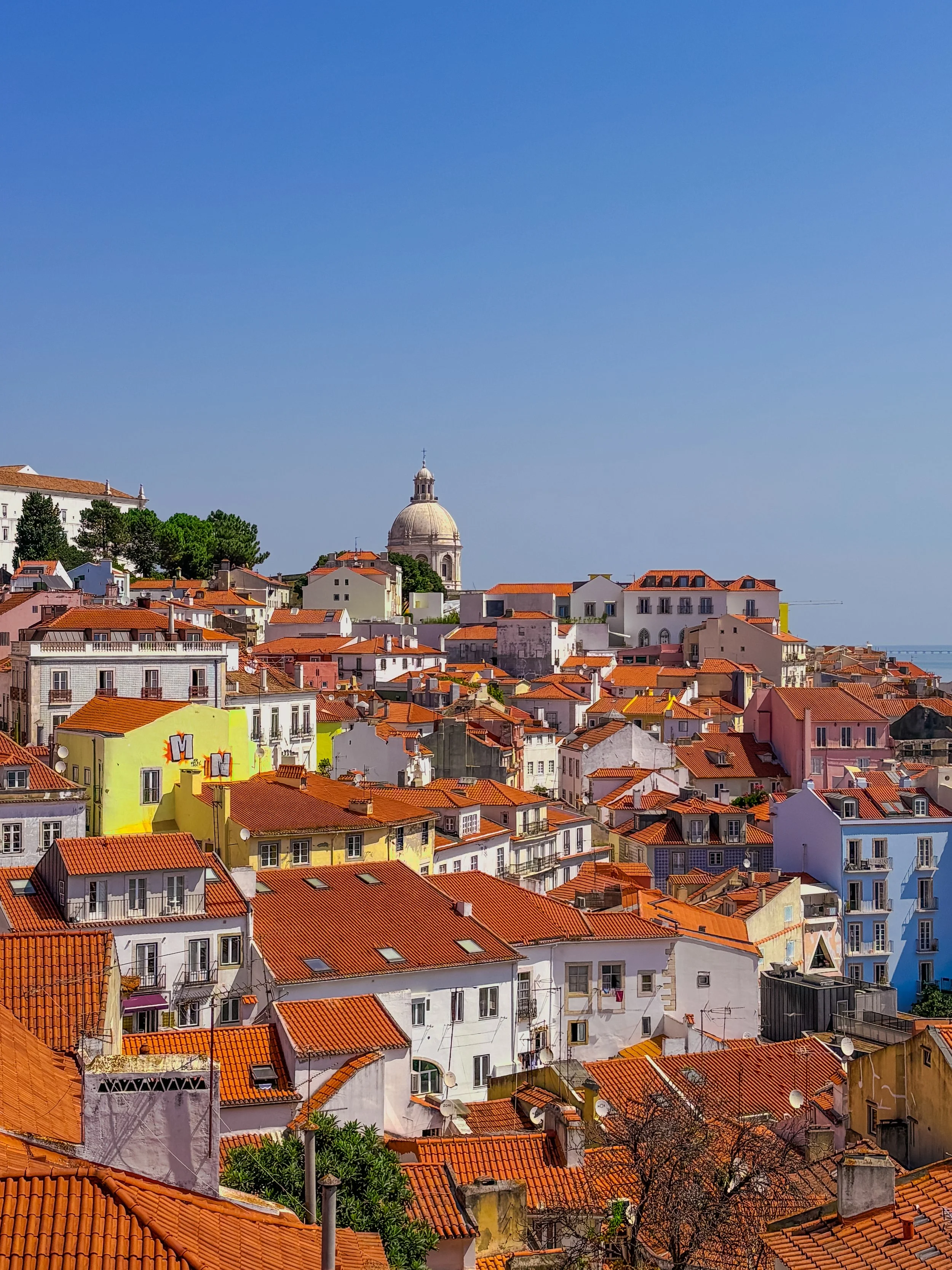 Colorful neighborhood with red-tiled rooftops and a domed church under a clear blue sky.