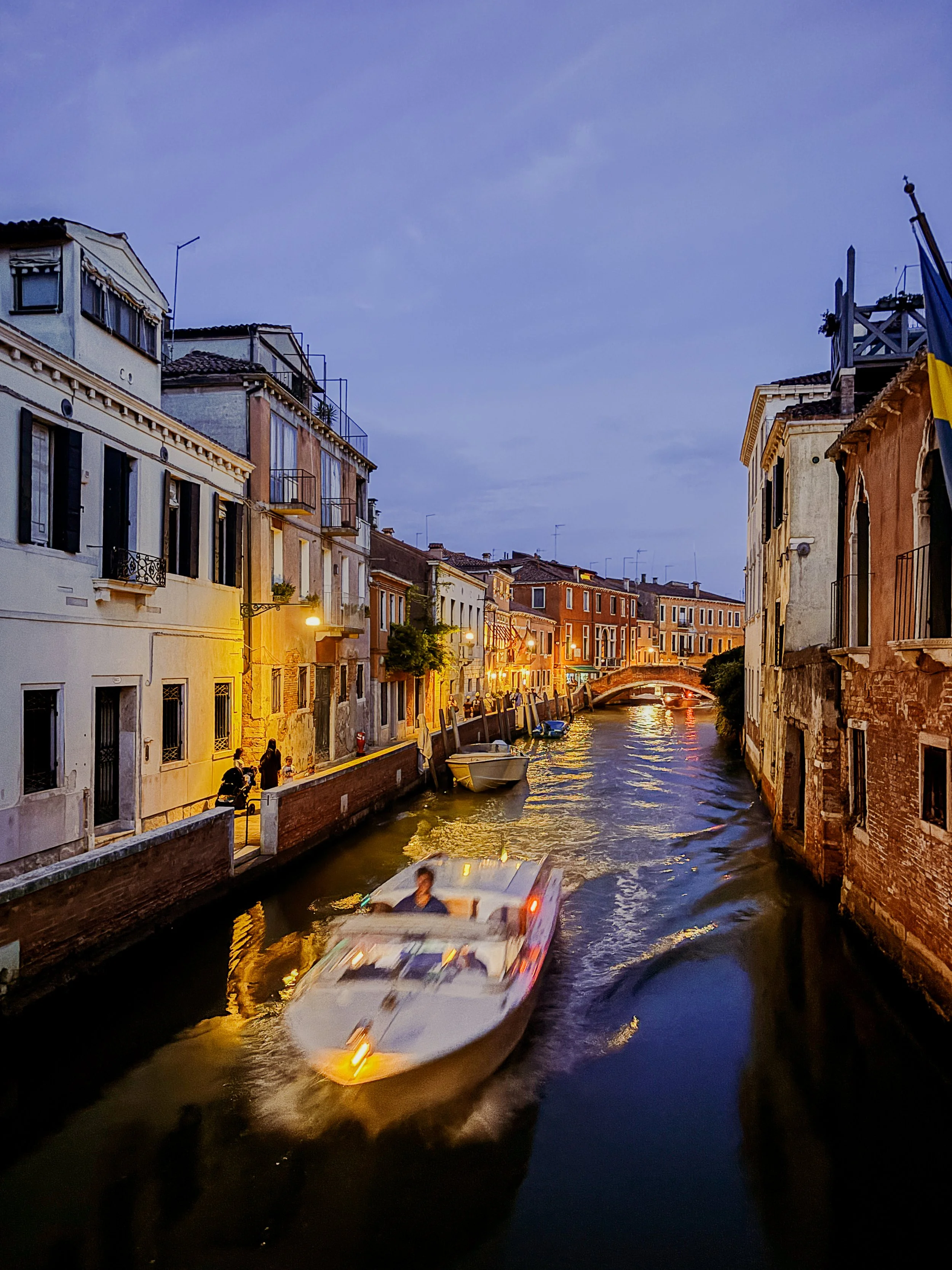 A canal in Venice at dusk with boats on the water and historic buildings along the sides.