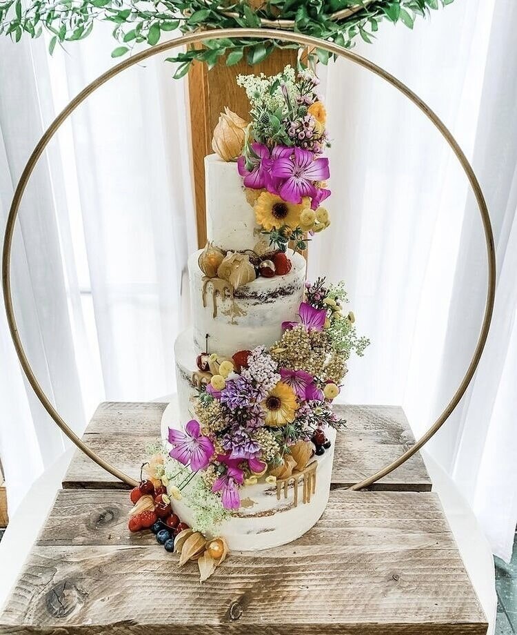 Semi naked four tier wedding cake with wild fresh flowers and a metal cake hoop stand.jpg