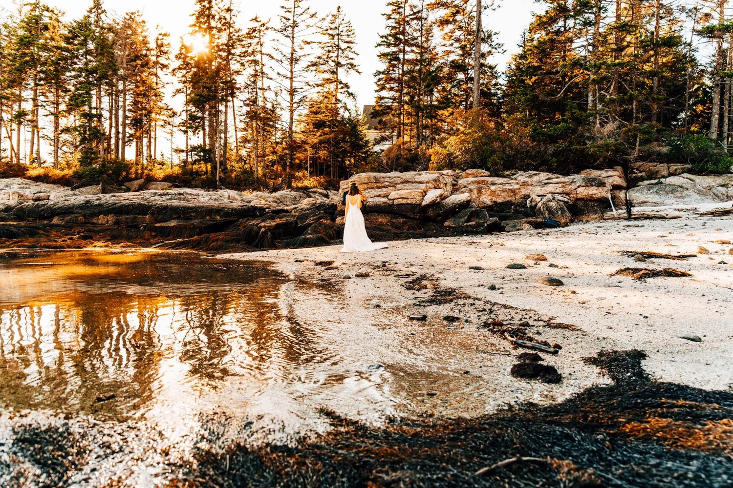 Bride walking the tide line on a quiet Maine beach, golden light reflecting in the shallow water