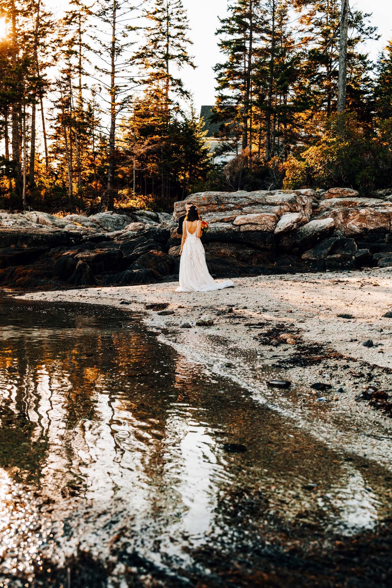 Bride walking toward the ledges on Pratts Island with the island house tucked into the spruce behind her