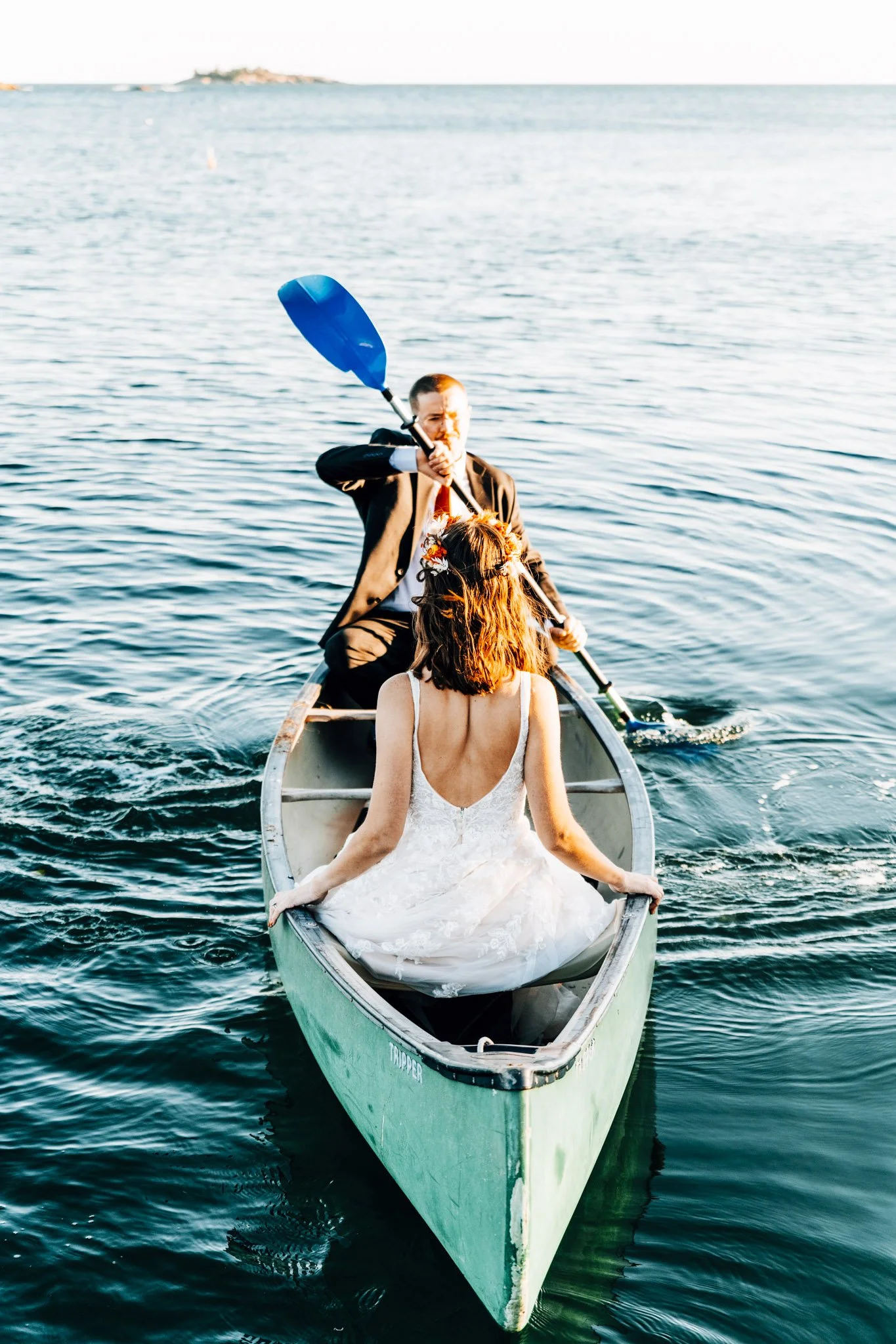 Alette and Kieron paddling a canoe off Pratts Island in their wedding clothes at golden hour