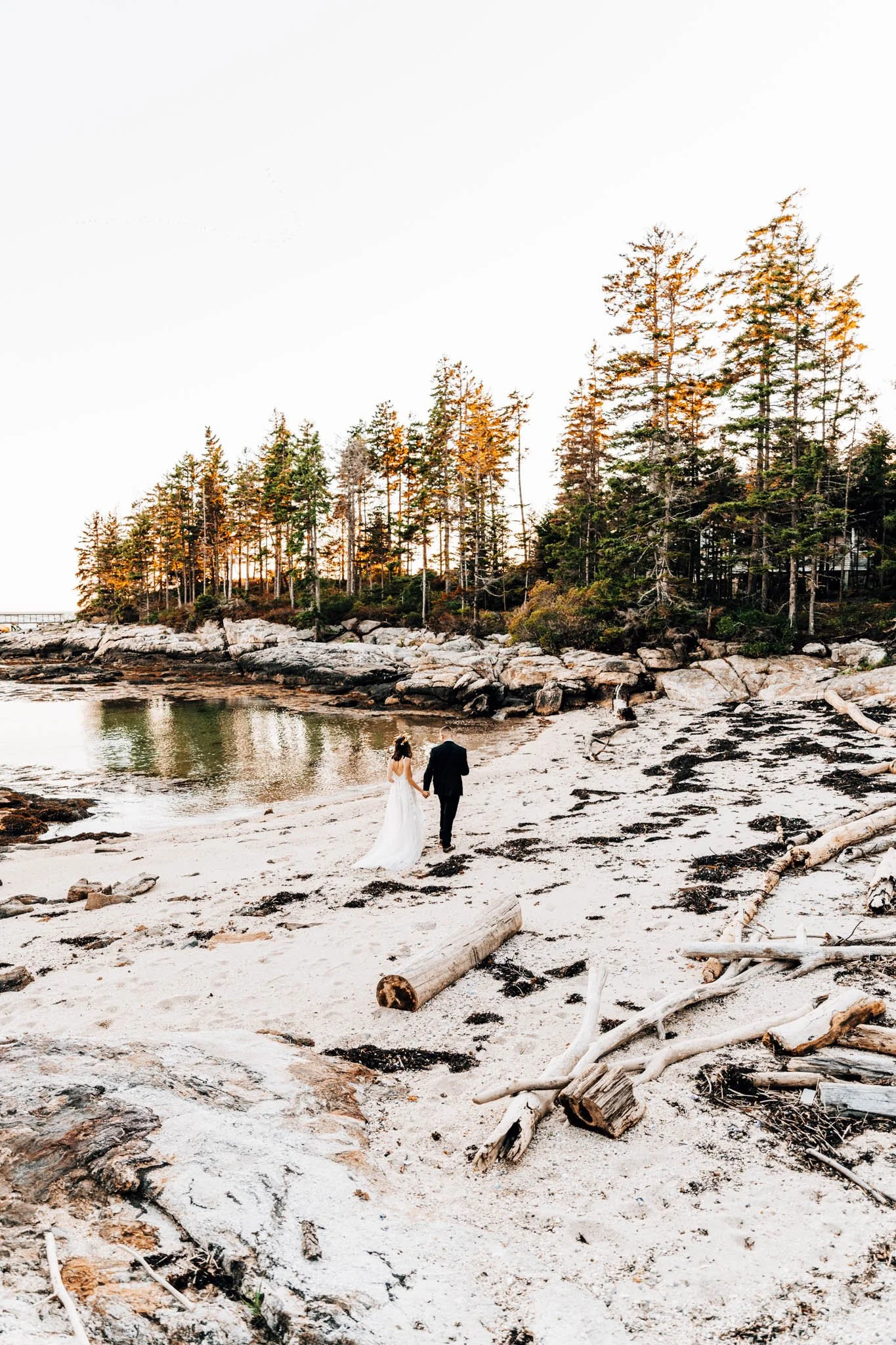 Couple walking a driftwood-strewn Maine beach toward a spruce point on Pratts Island