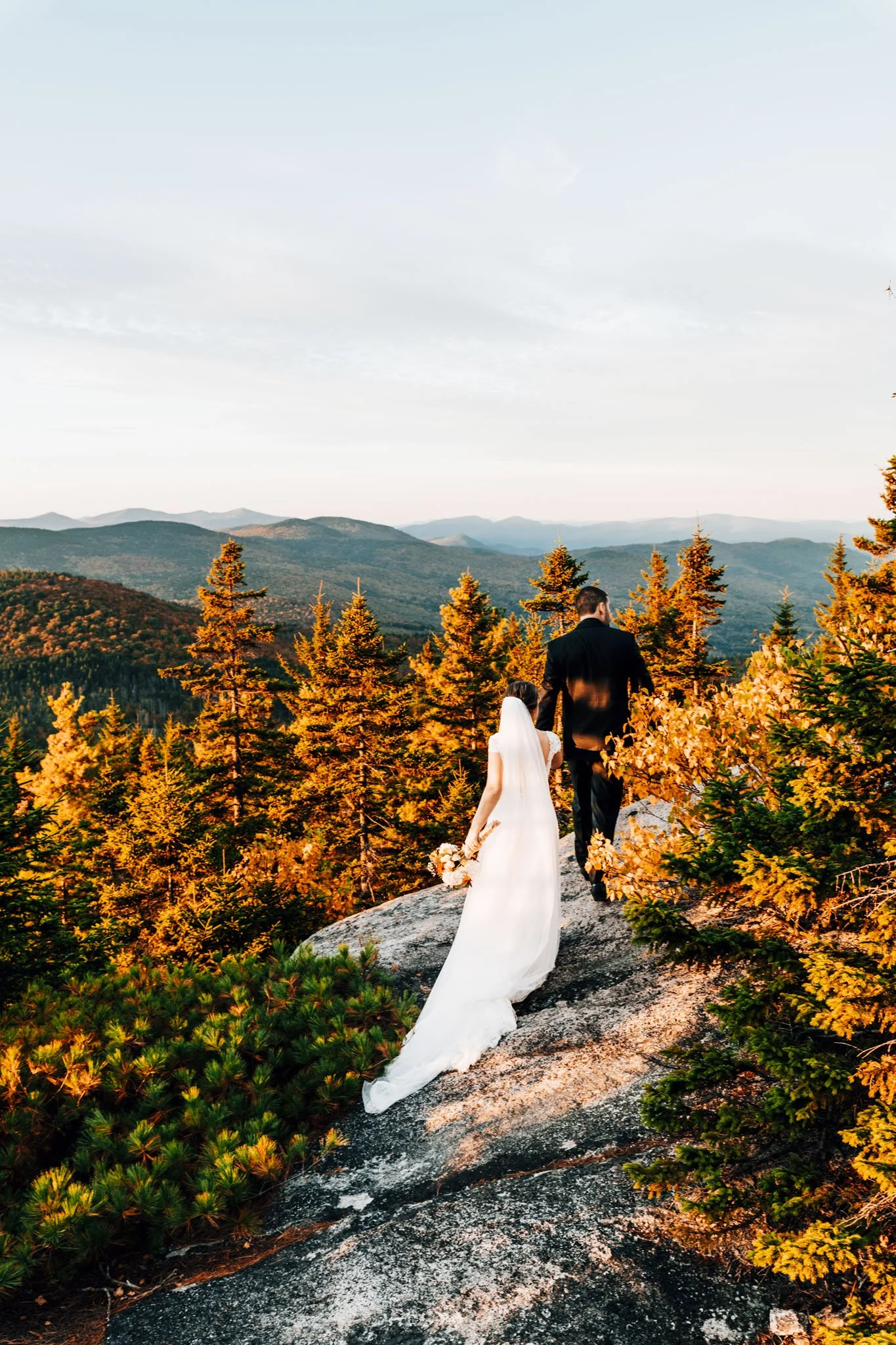 Bride's veil trailing behind her as the couple walks toward the overlook on Black Cap, peak foliage filling the valley below