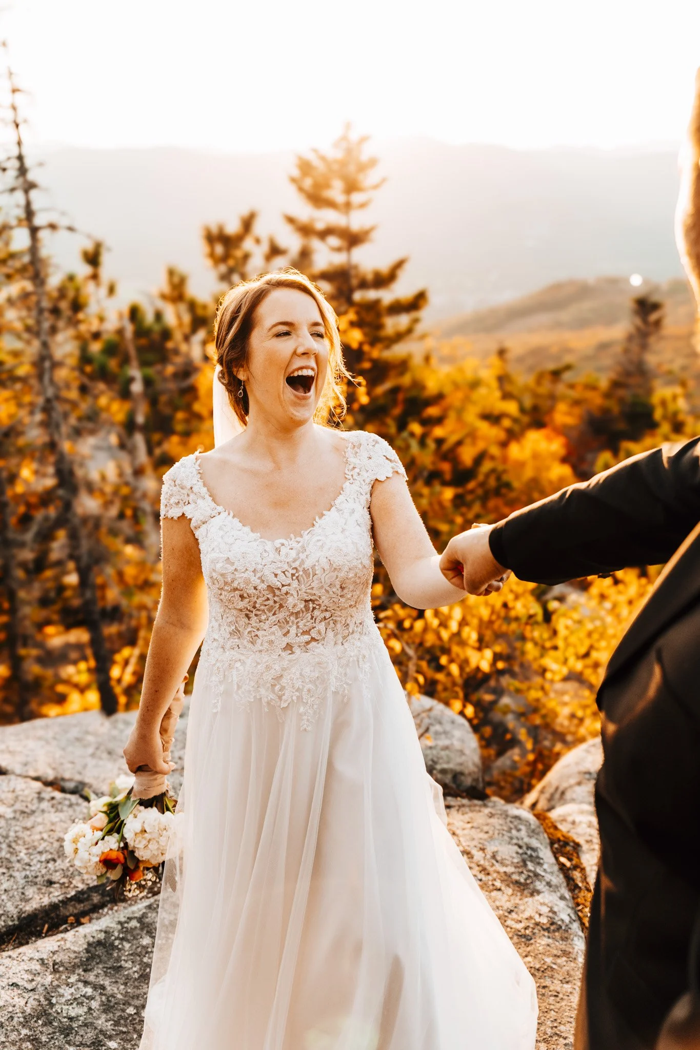 Bride laughing with her whole face as she holds her groom's hand on the Black Cap summit in golden October light