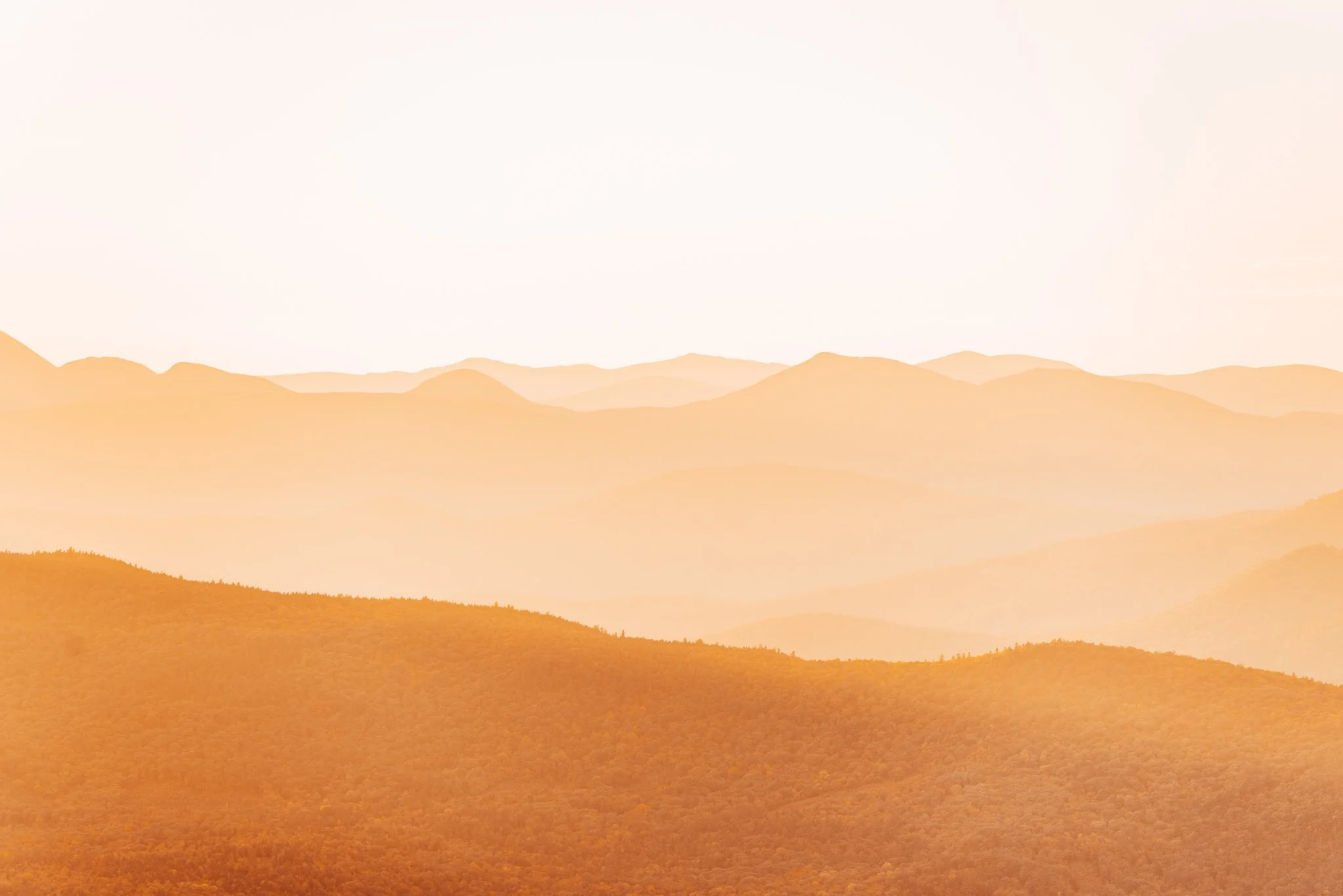 Layered White Mountain ridgelines glowing hazy orange at sunset, seen from Black Cap Mountain