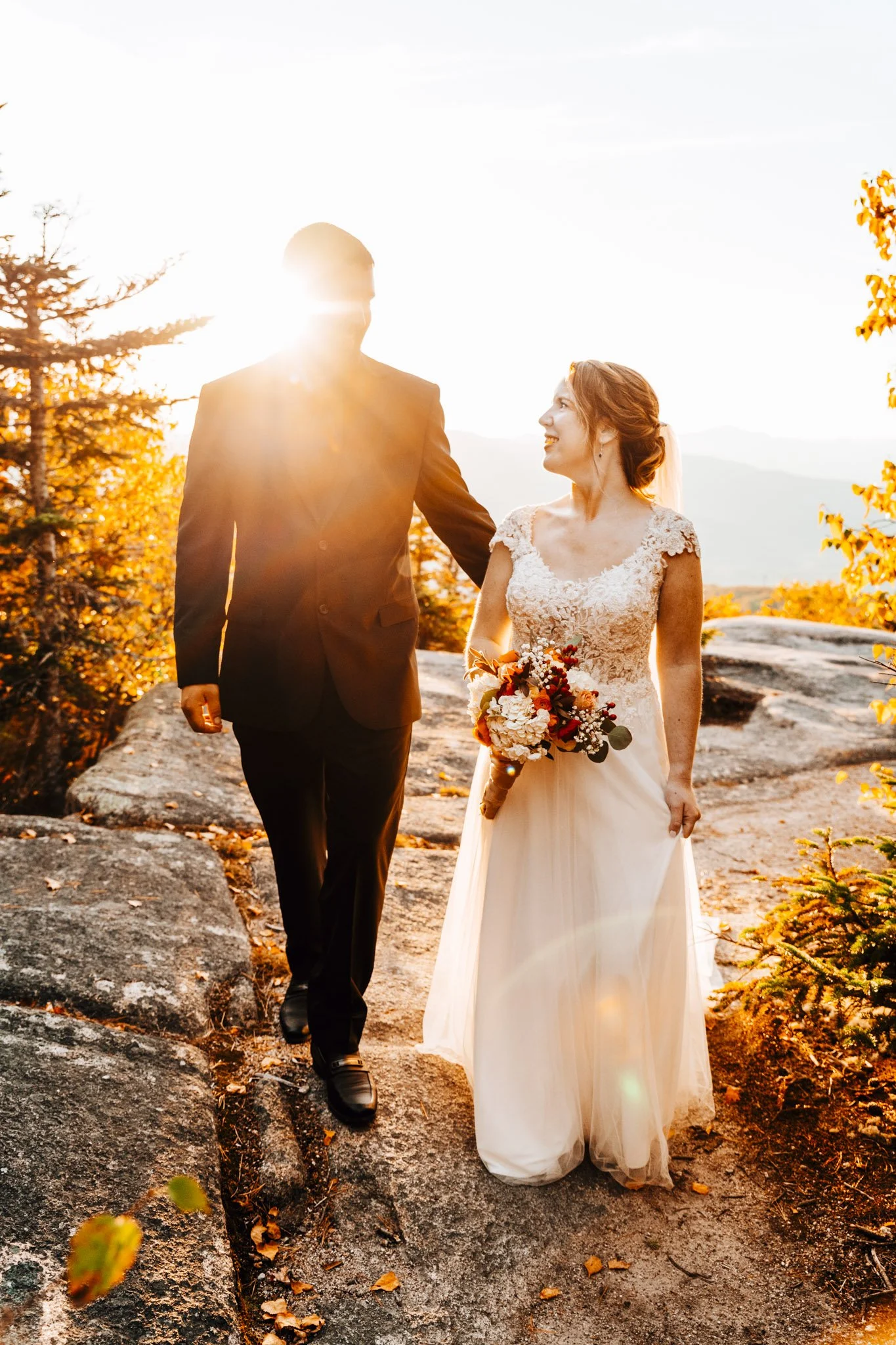 Annalise and Josh walking hand in hand across granite in golden October light above North Conway, New Hampshire