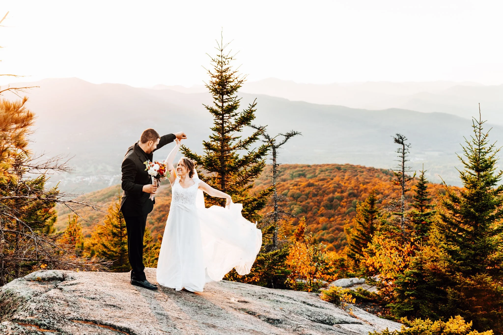Groom spinning his bride's dress on the open ledge of Black Cap with the fall valley of North Conway behind them