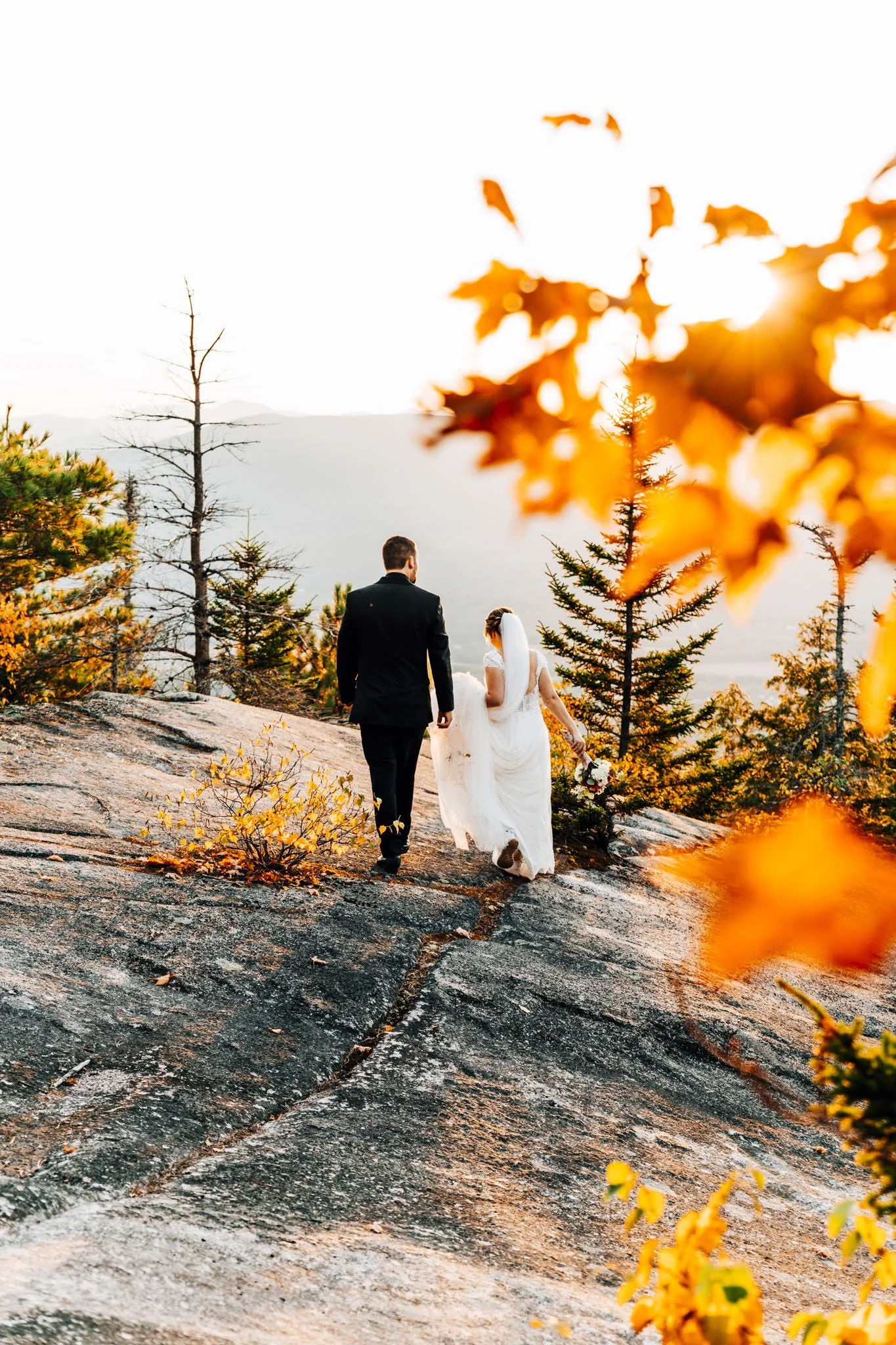 Annalise and Josh walking up the granite slab of Black Cap framed by burnt orange oak leaves