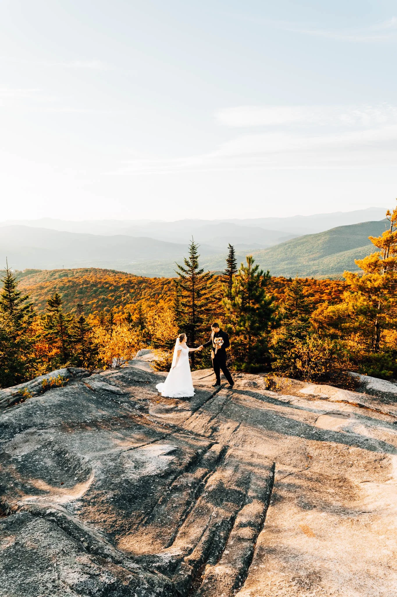 Annalise and Josh alone on a wide granite slab above miles of peak foliage in the White Mountains