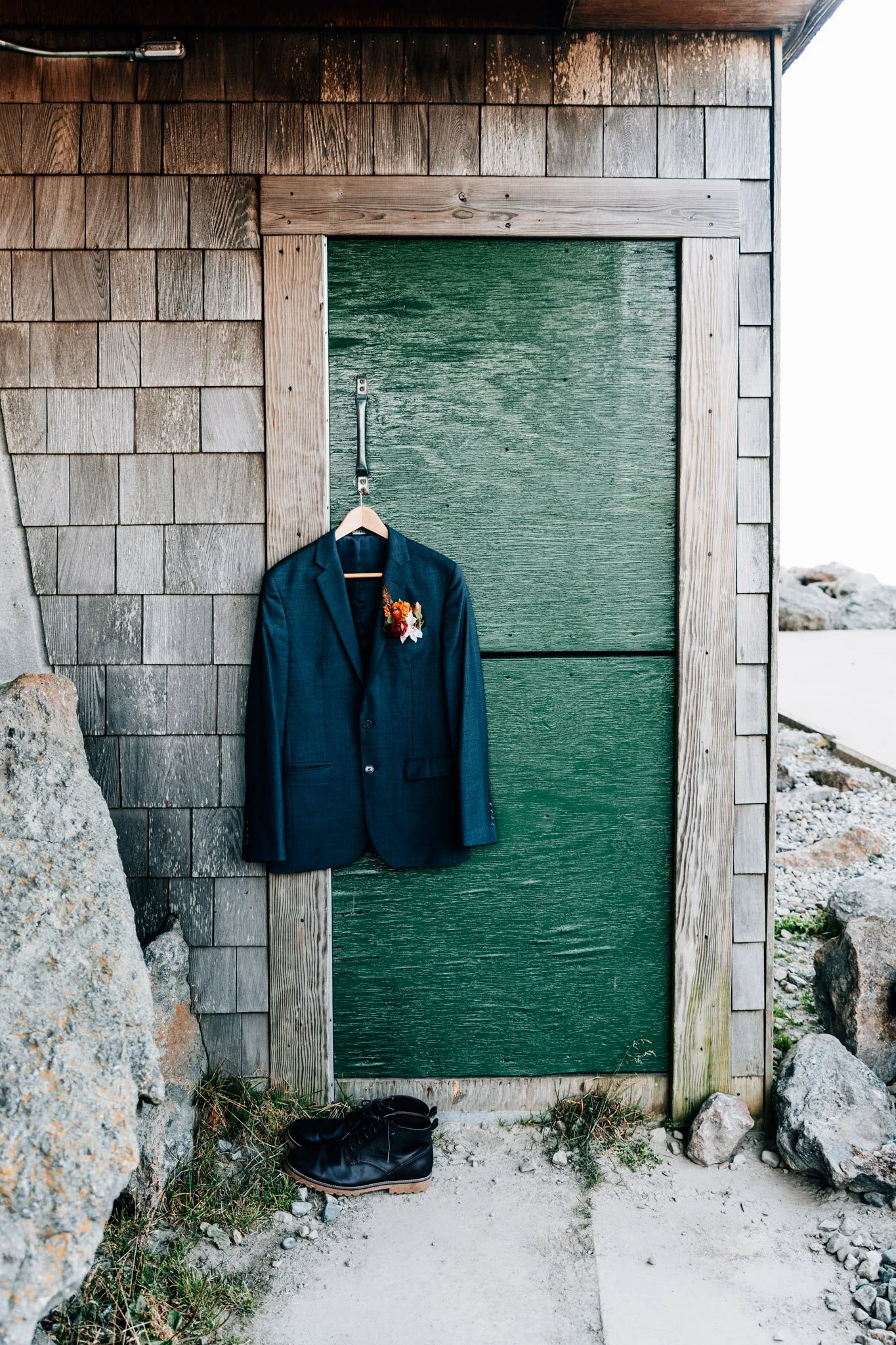 Groom's navy suit and dried autumn boutonniere hanging on the weathered green door of a Mount Washington summit building