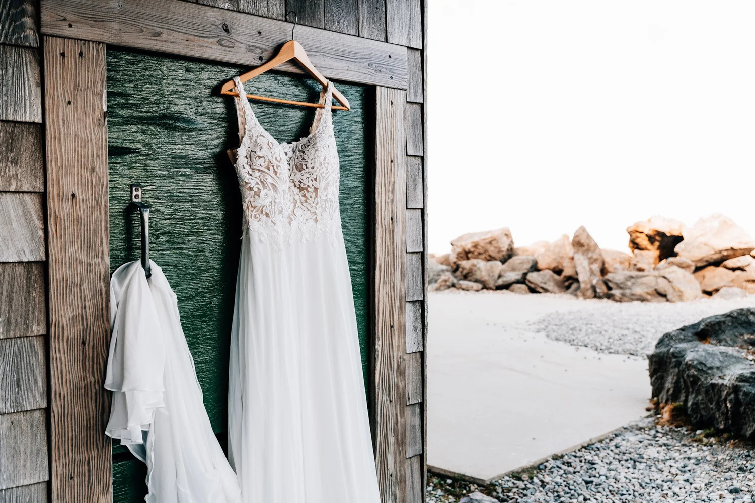 Lace and chiffon wedding dress hanging on a weathered green door at the summit of Mount Washington, veil on a hook beside it