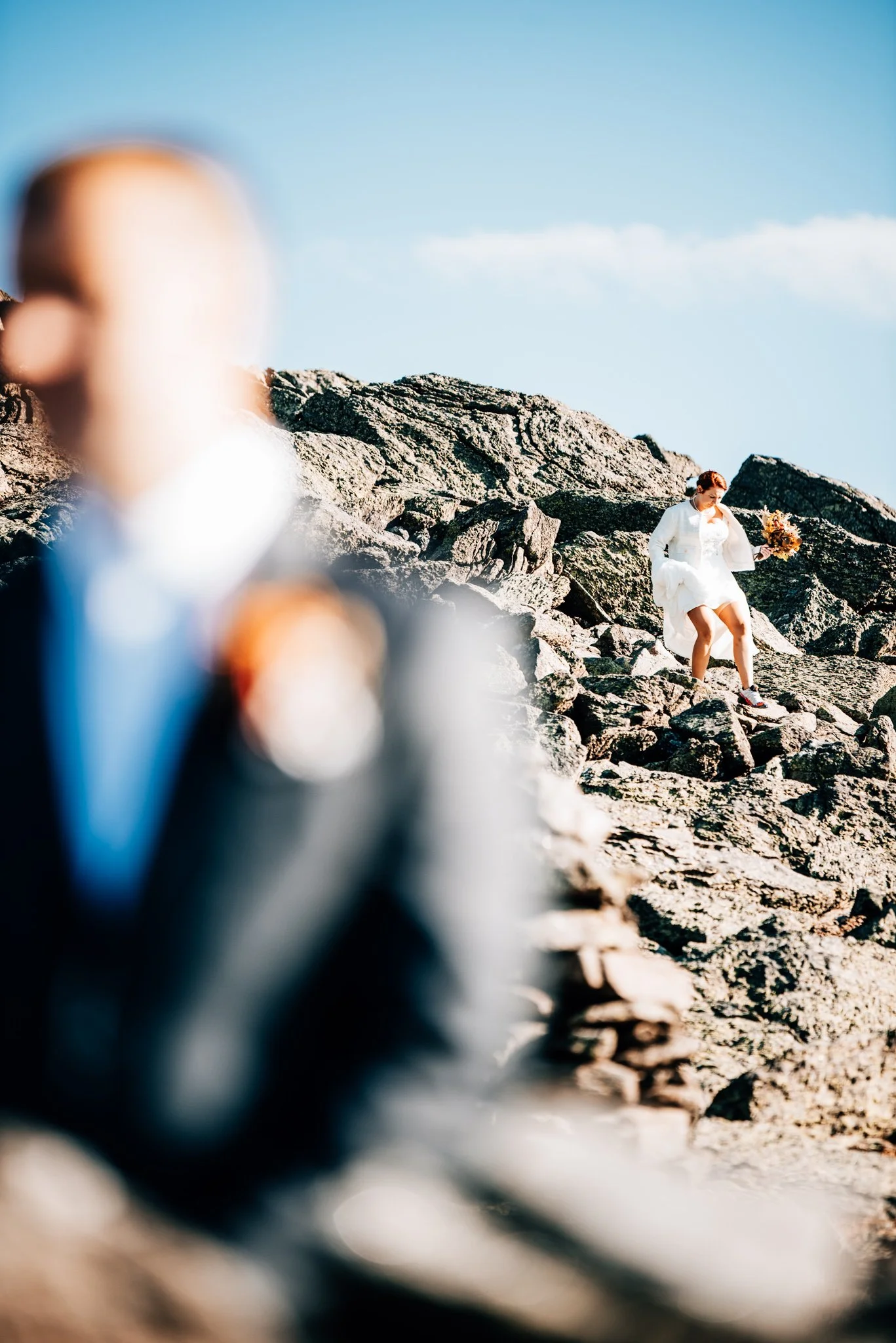 First look off the Jewell Trail, the groom blurred in the foreground as his bride steps down through the summit boulders