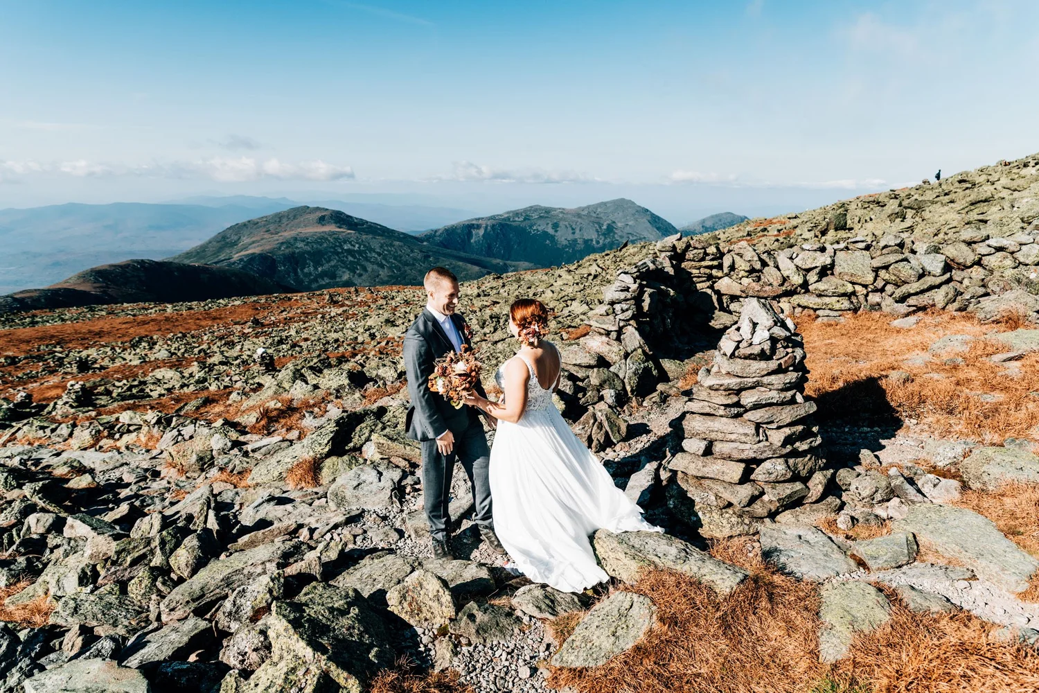 Danielle and Tom beside a stone cairn on the Mount Washington summit cone with the Presidential Range behind them