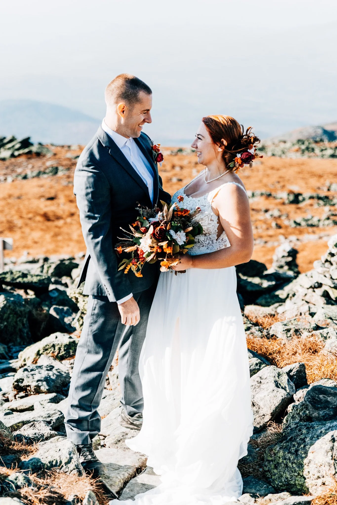 Bride and groom laughing face to face among the golden alpine grass and rock of the Mount Washington summit