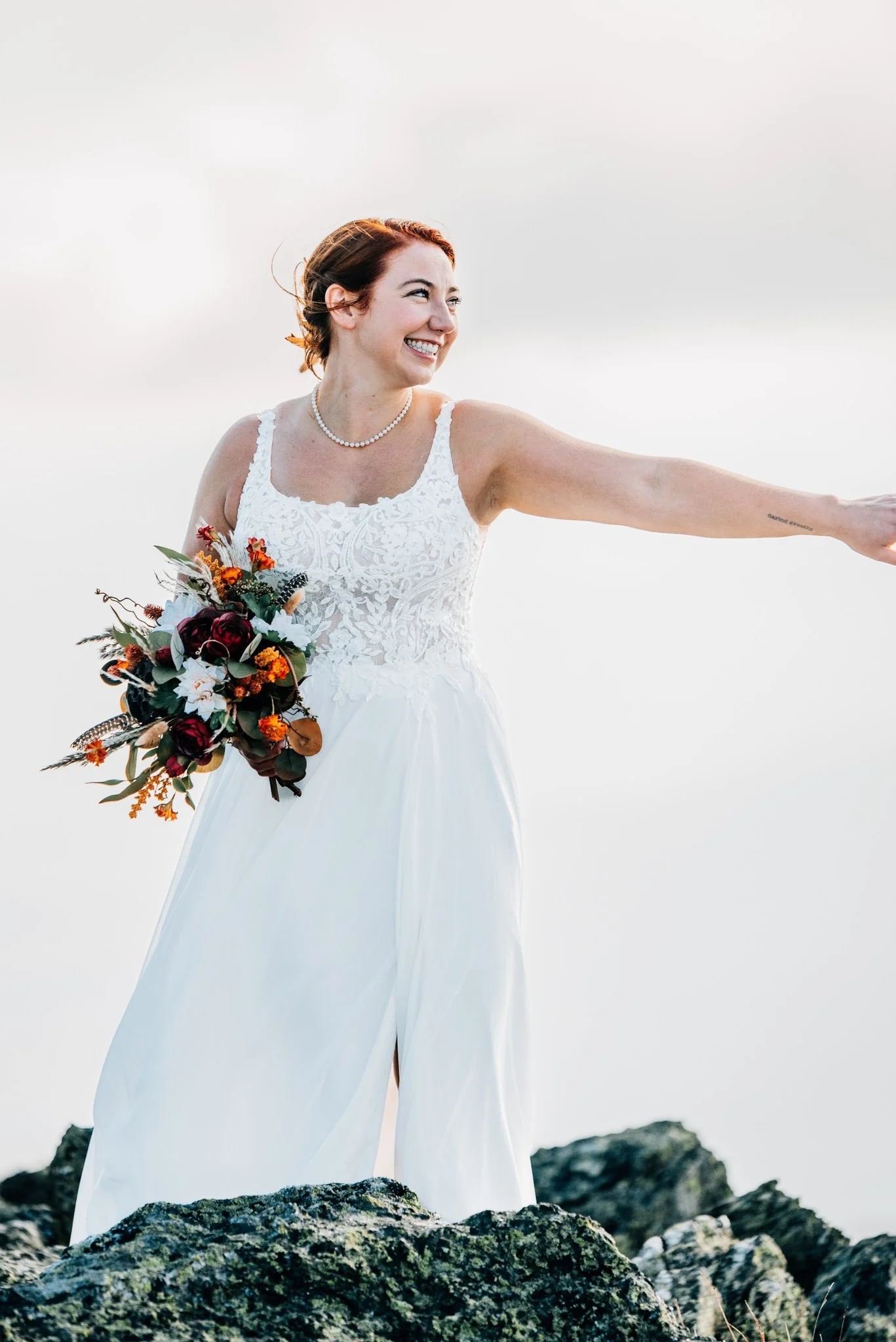 Bride laughing in a lace bodice gown, reaching out for her partner's hand on the Mount Washington summit