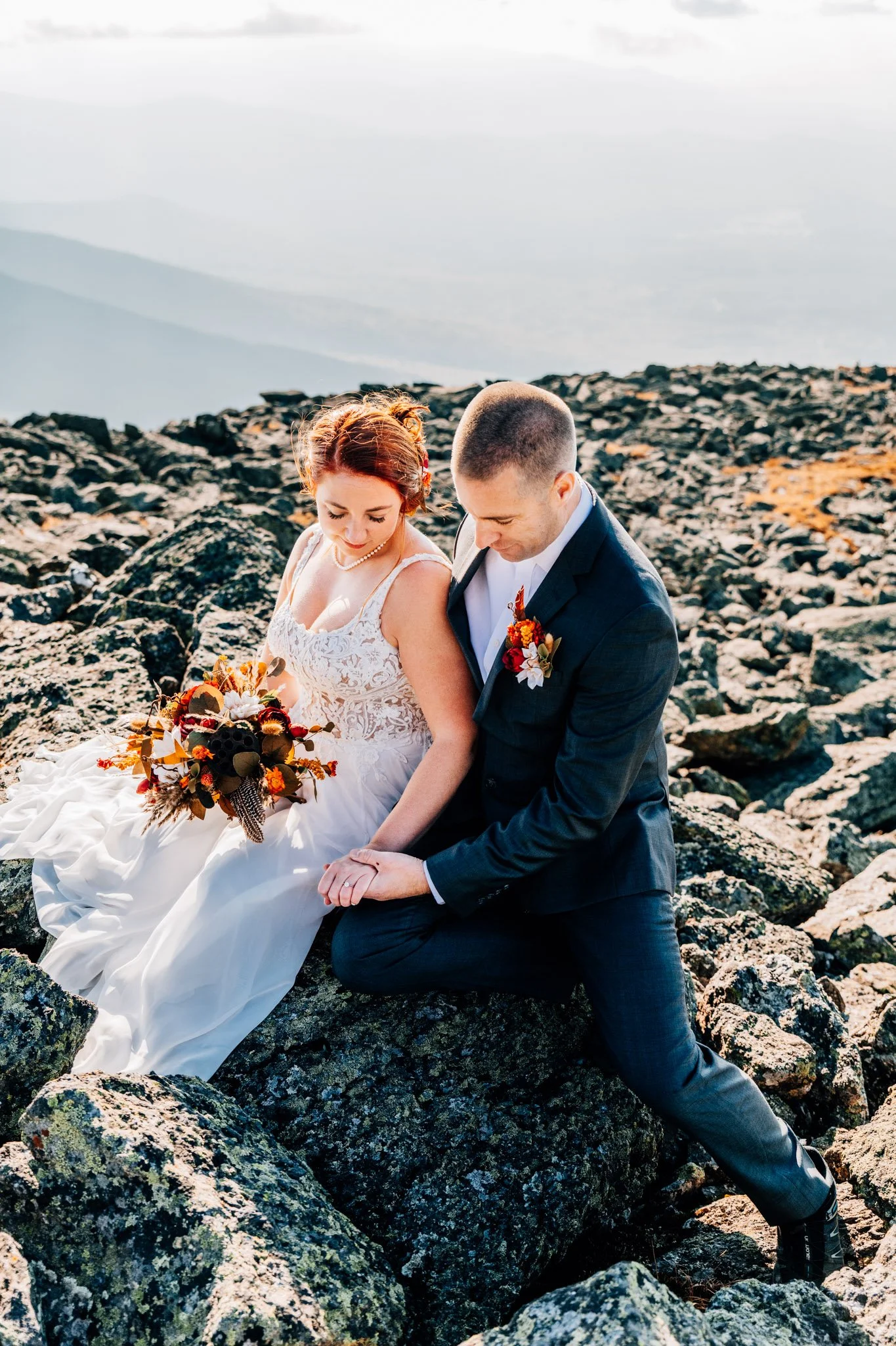 Danielle and Tom sitting together on the Mount Washington boulder field, hands held and heads bowed