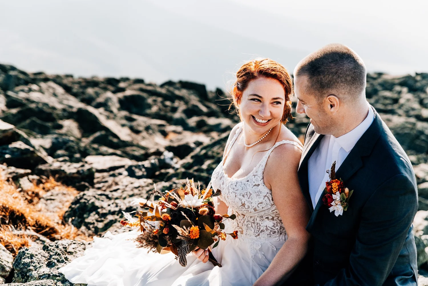 Close portrait of the bride smiling with her autumn bouquet, her groom beside her on the summit