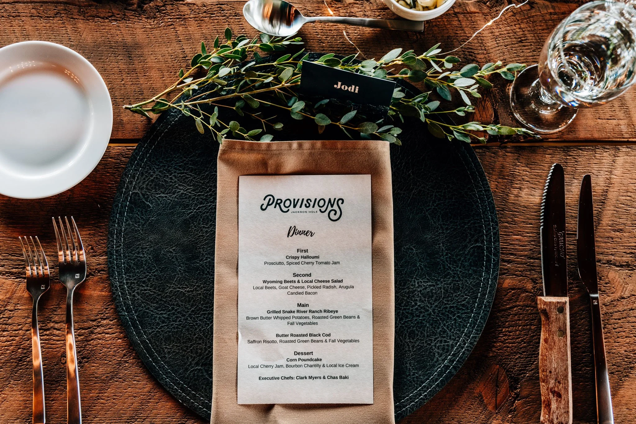 Place setting with a printed dinner menu, greenery and a name card at a Jackson Hole wedding dinner