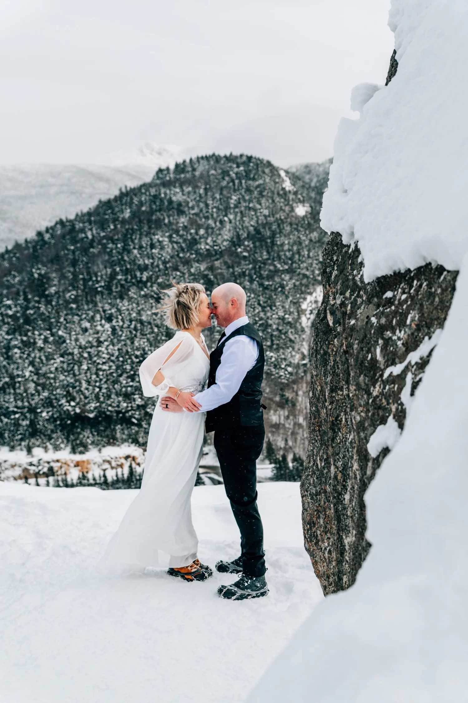 Bride and groom kissing in fresh snow above a mountain notch, winter elopement in New Hampshire