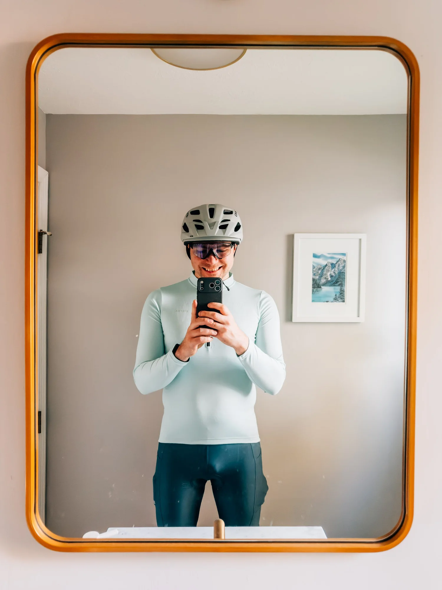 Smiling cyclist in a helmet, sunglasses and pale blue jersey taking a mirror selfie before a road ride