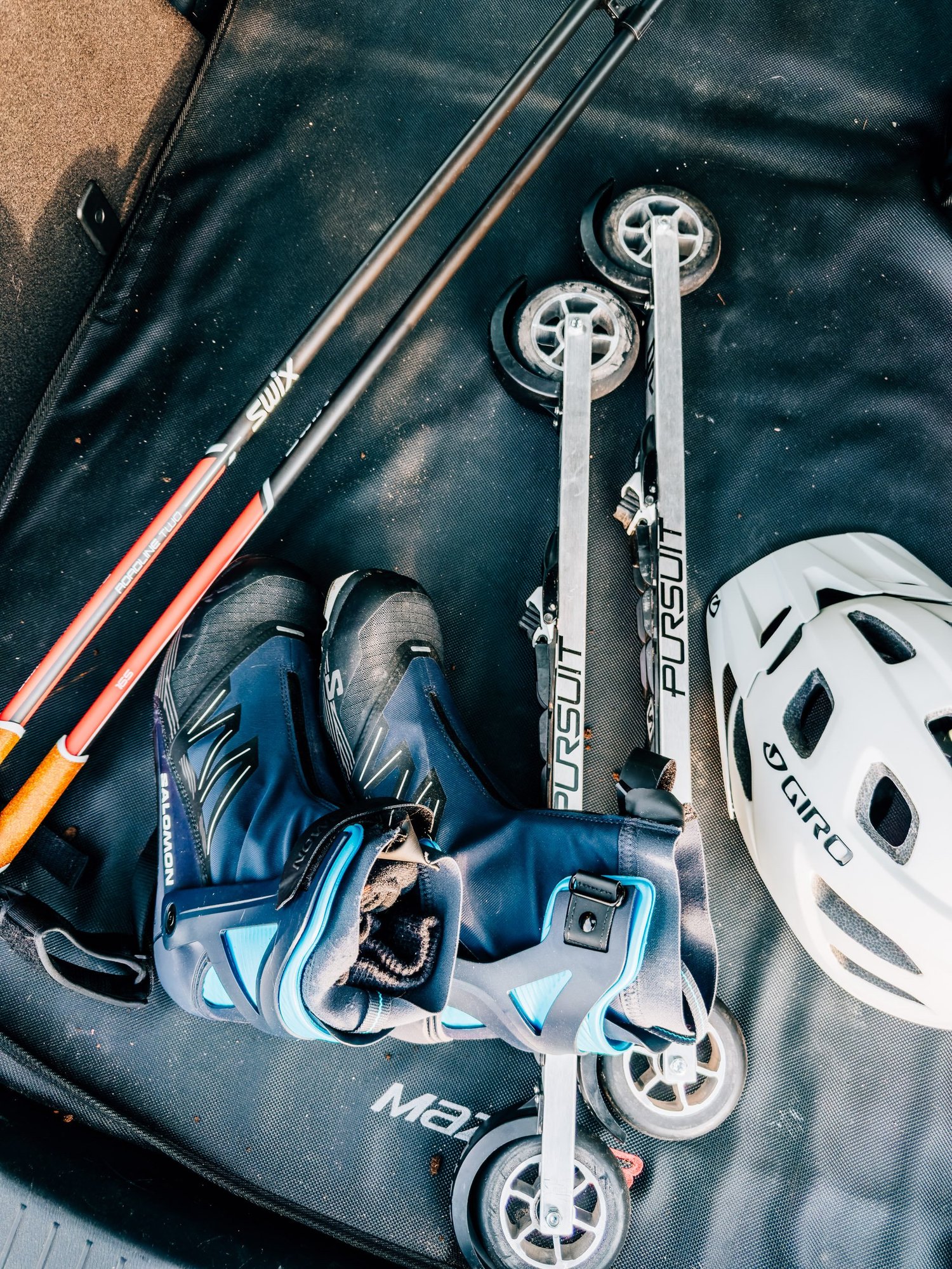 Roller skis, ski poles, boots and a helmet laid out on a black mat in the back of a car