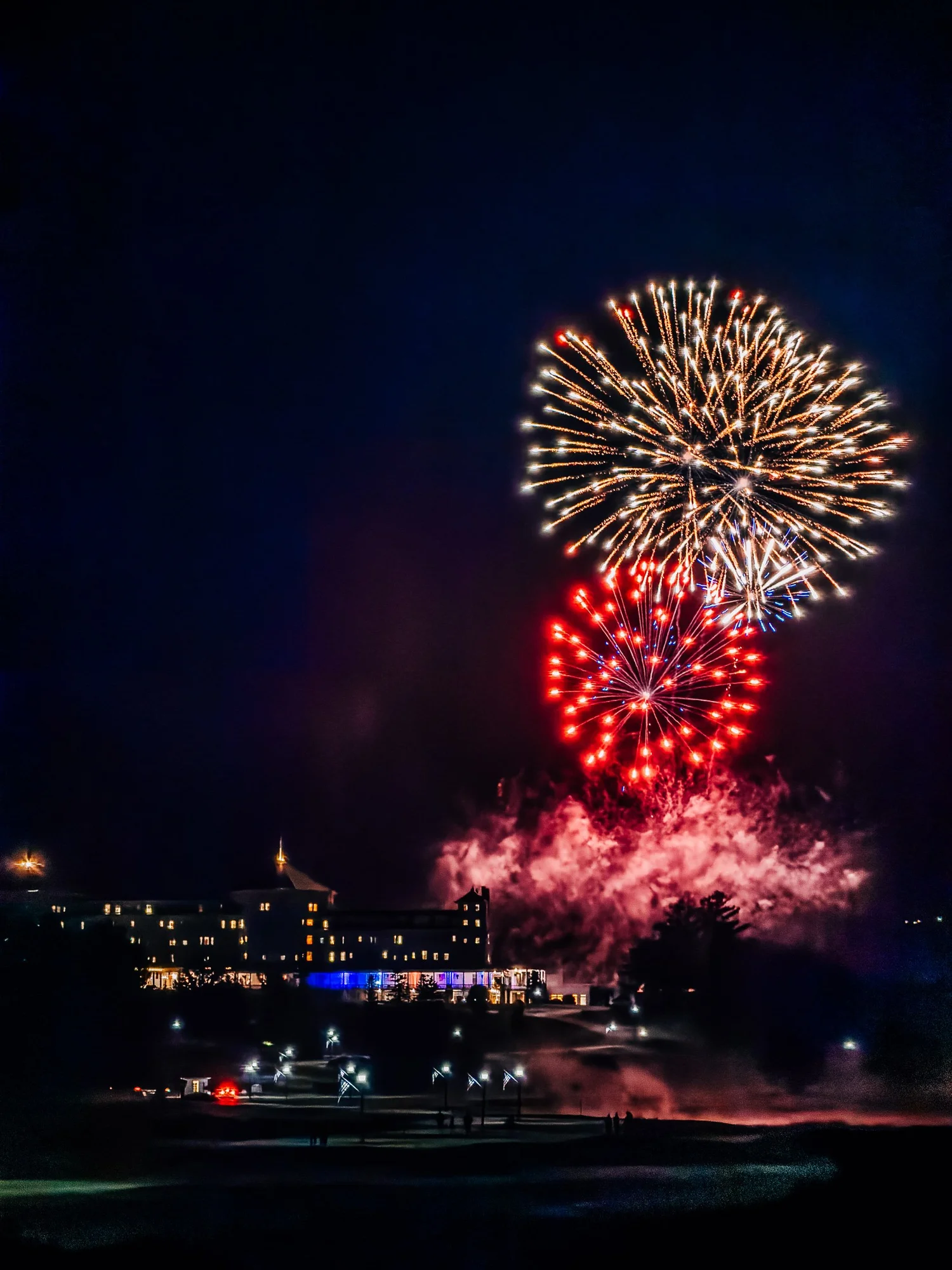 Gold and red fireworks bursting over the lit-up Mount Washington Hotel against a night sky