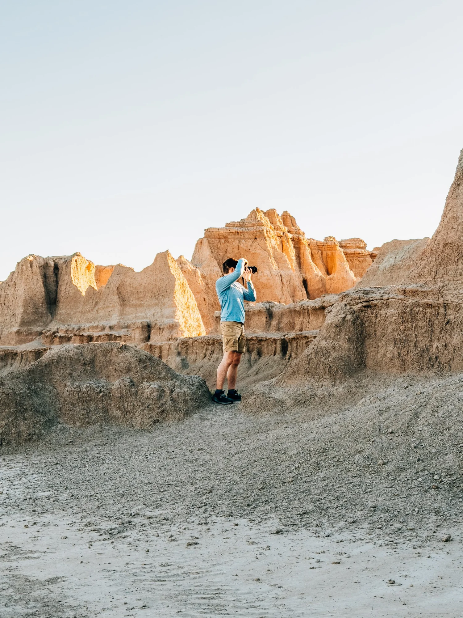 Photographer in a blue shirt raising a camera among glowing orange Badlands formations at sunrise